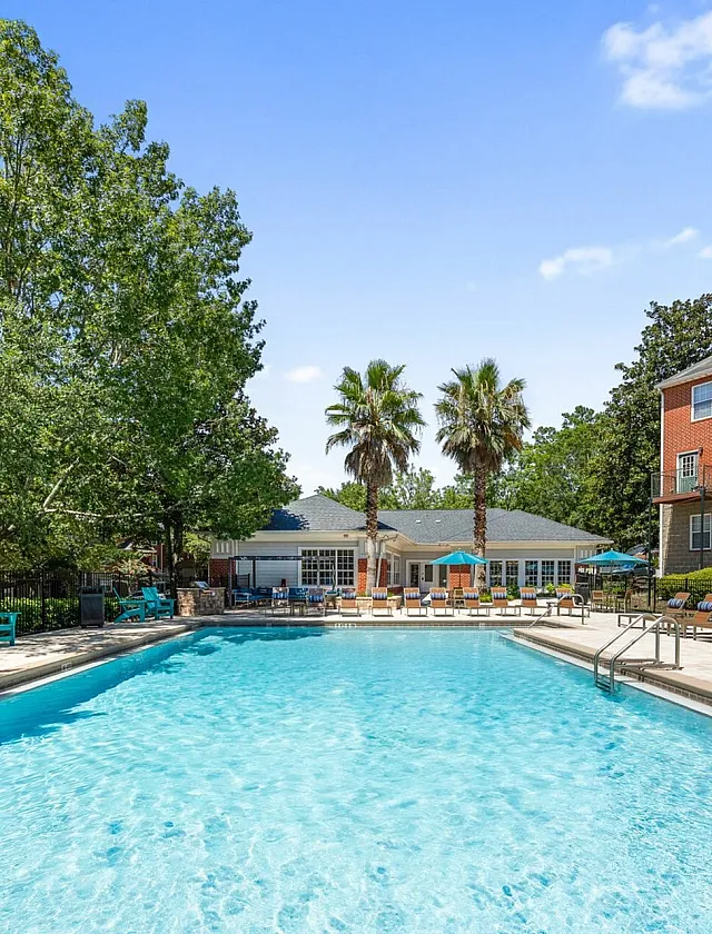 Inviting apartment community with a sparkling swimming pool, surrounded by lush greenery and comfortable lounge chairs, perfect for relaxation and leisure.