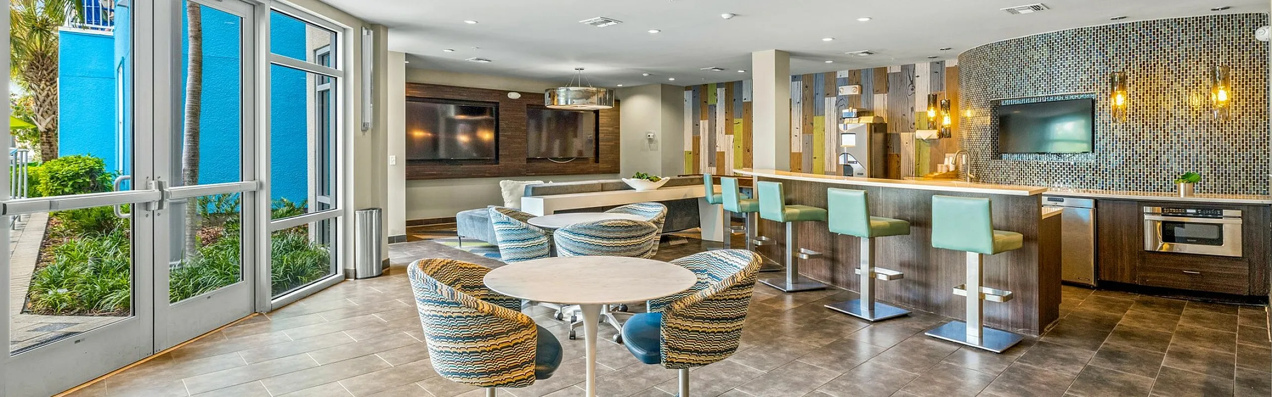Modern communal lounge with vibrant decor, featuring a spacious bar, cozy seating areas, large windows, and sleek design elements.