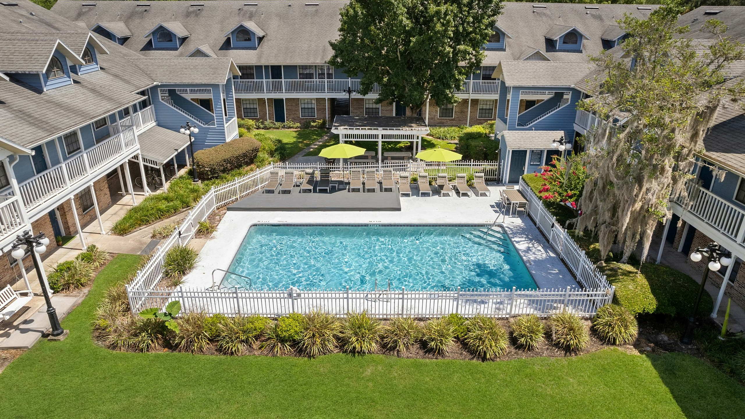 Charming apartment complex with a pristine outdoor pool, sun loungers, and lush greenery, offering a relaxing lifestyle retreat.