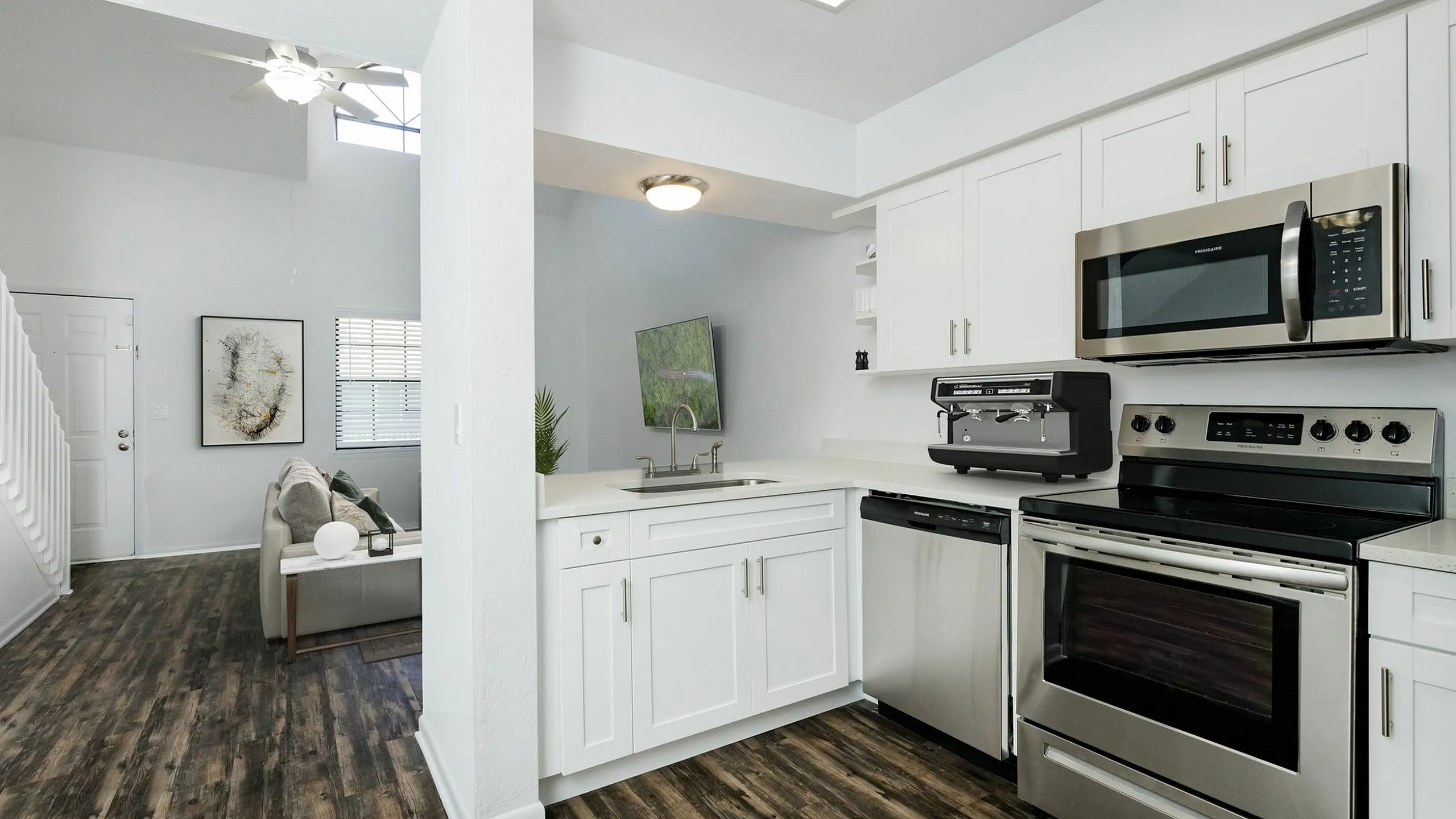 Modern apartment interior showcasing a sleek kitchen with stainless steel appliances and bright, open living area featuring stylish decor and wood flooring.