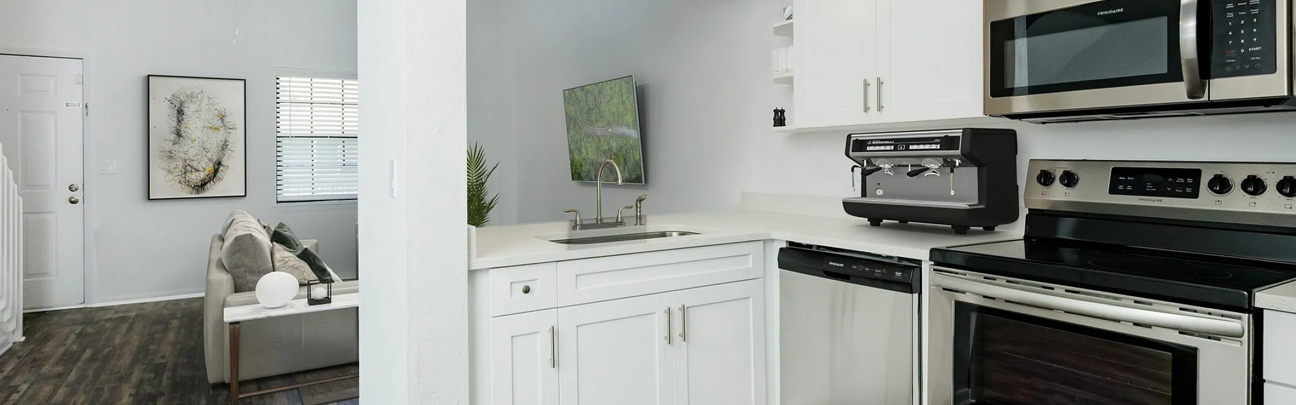 Modern open-concept kitchen with sleek stainless steel appliances and cozy adjoining living room, featuring elegant wood flooring and bright white cabinetry.