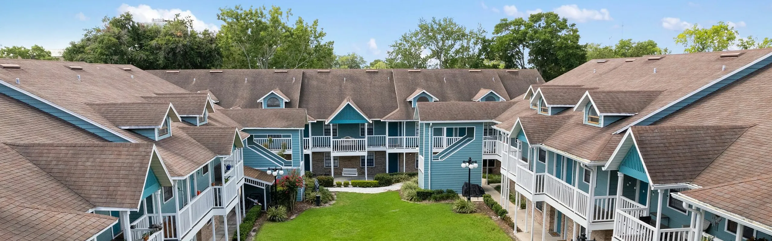 Charming apartment complex featuring blue and white two-story buildings with welcoming balconies and a lush green courtyard.