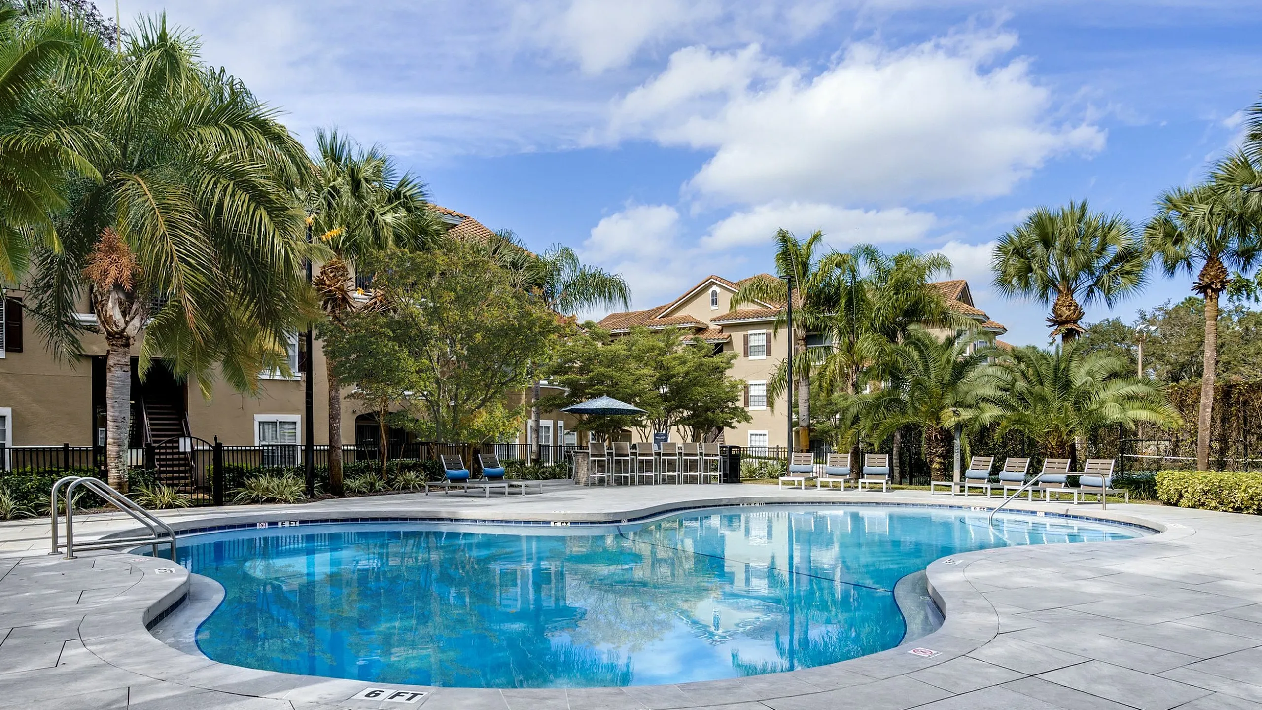 Luxurious apartment complex featuring a sparkling pool surrounded by lush palm trees and elegant lounge chairs, perfect for relaxation.