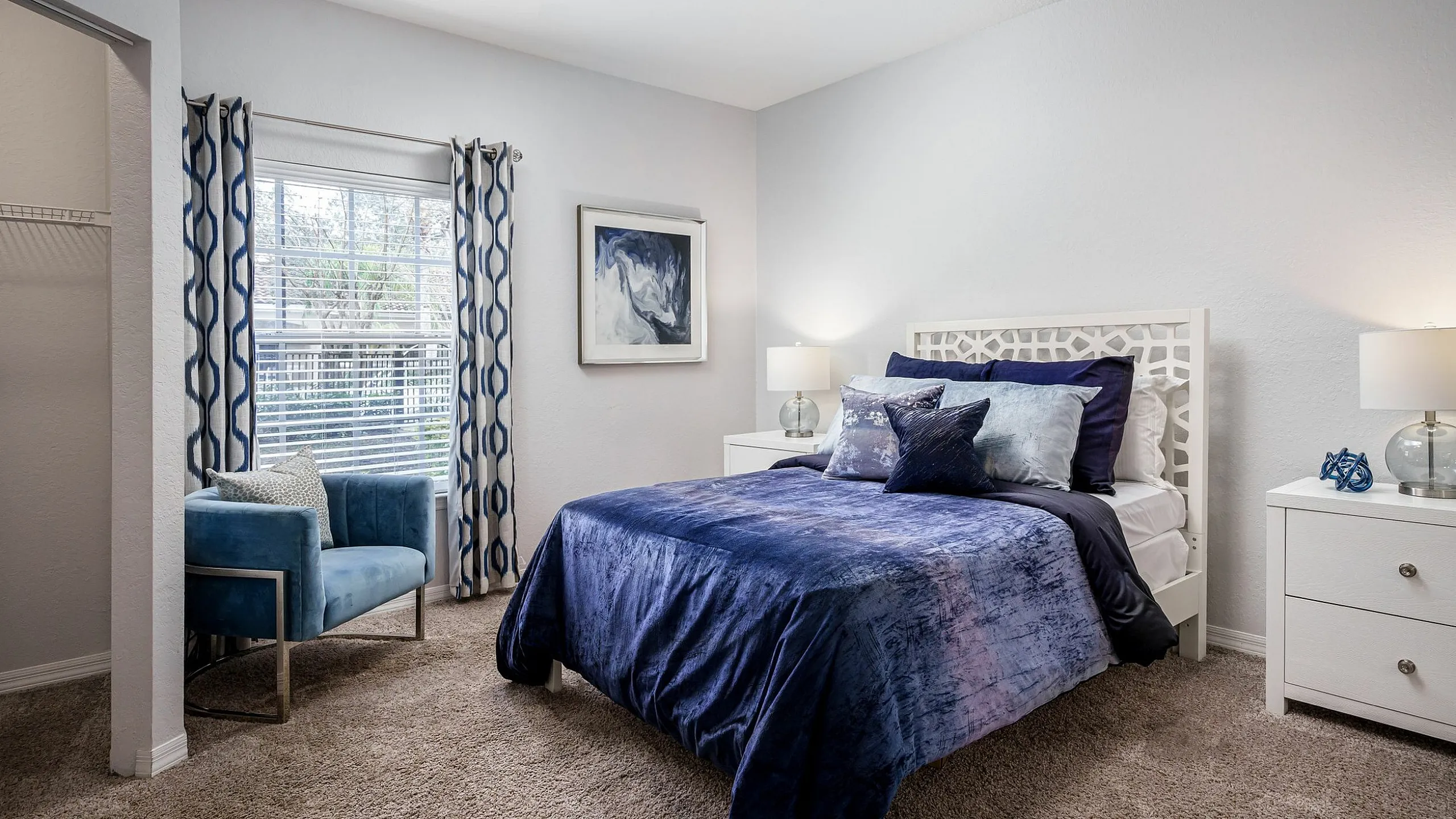 Elegant bedroom with a blue and white theme, featuring a cozy bed, stylish armchair, and natural light from large windows.