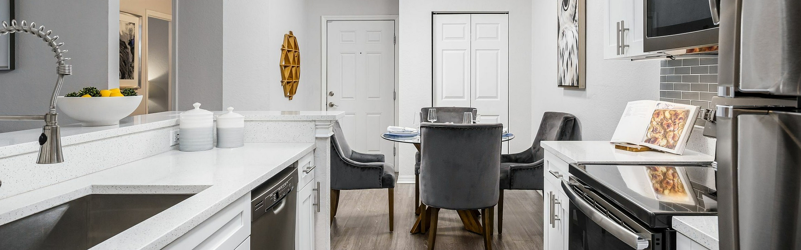 Modern kitchen with sleek stainless steel appliances, elegant white cabinetry, and a cozy dining area featuring plush gray chairs.