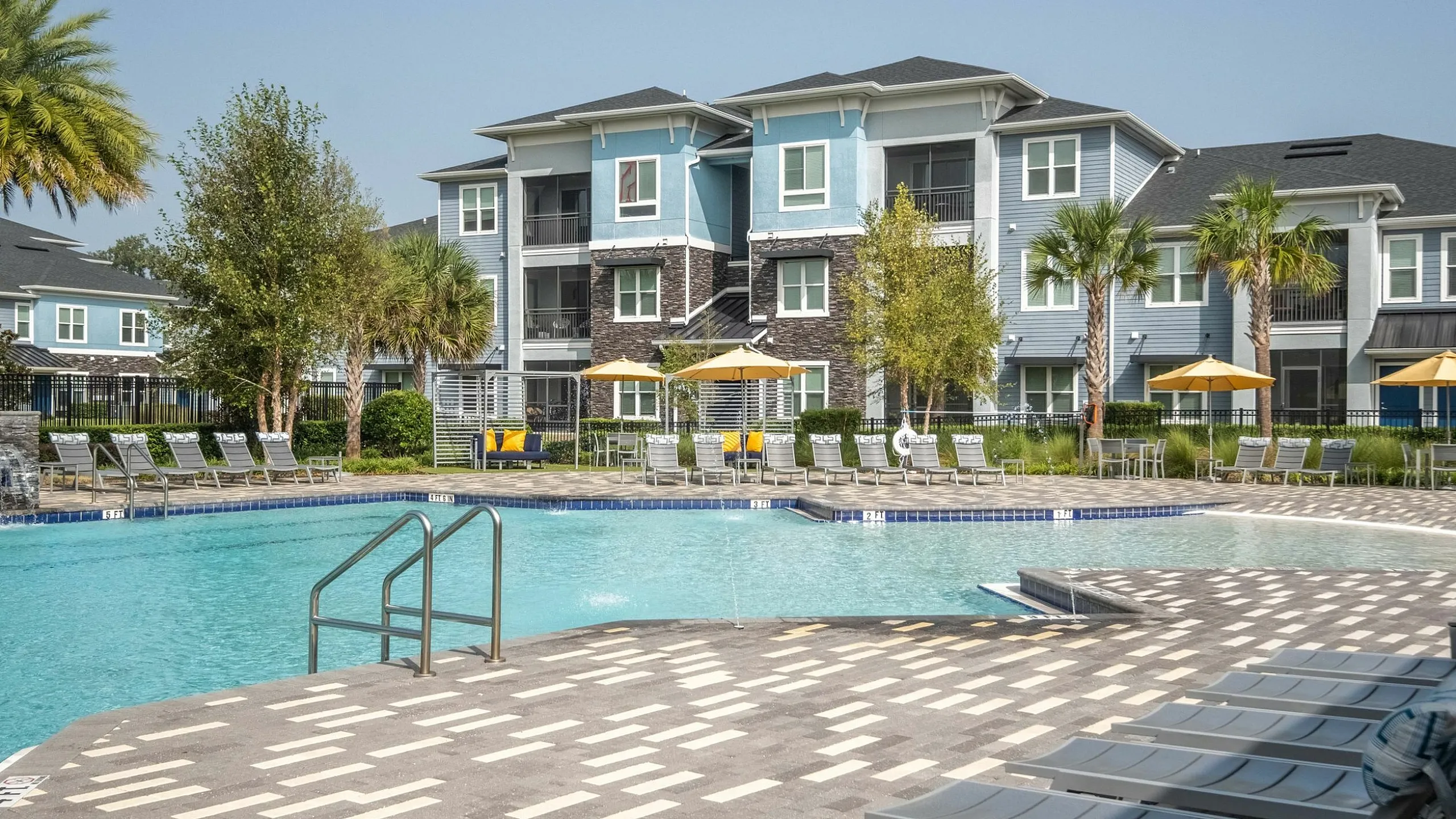 Luxury apartment complex with a stunning outdoor pool area, surrounded by stylish lounge chairs and vibrant umbrellas, set against modern architecture and lush palm trees.