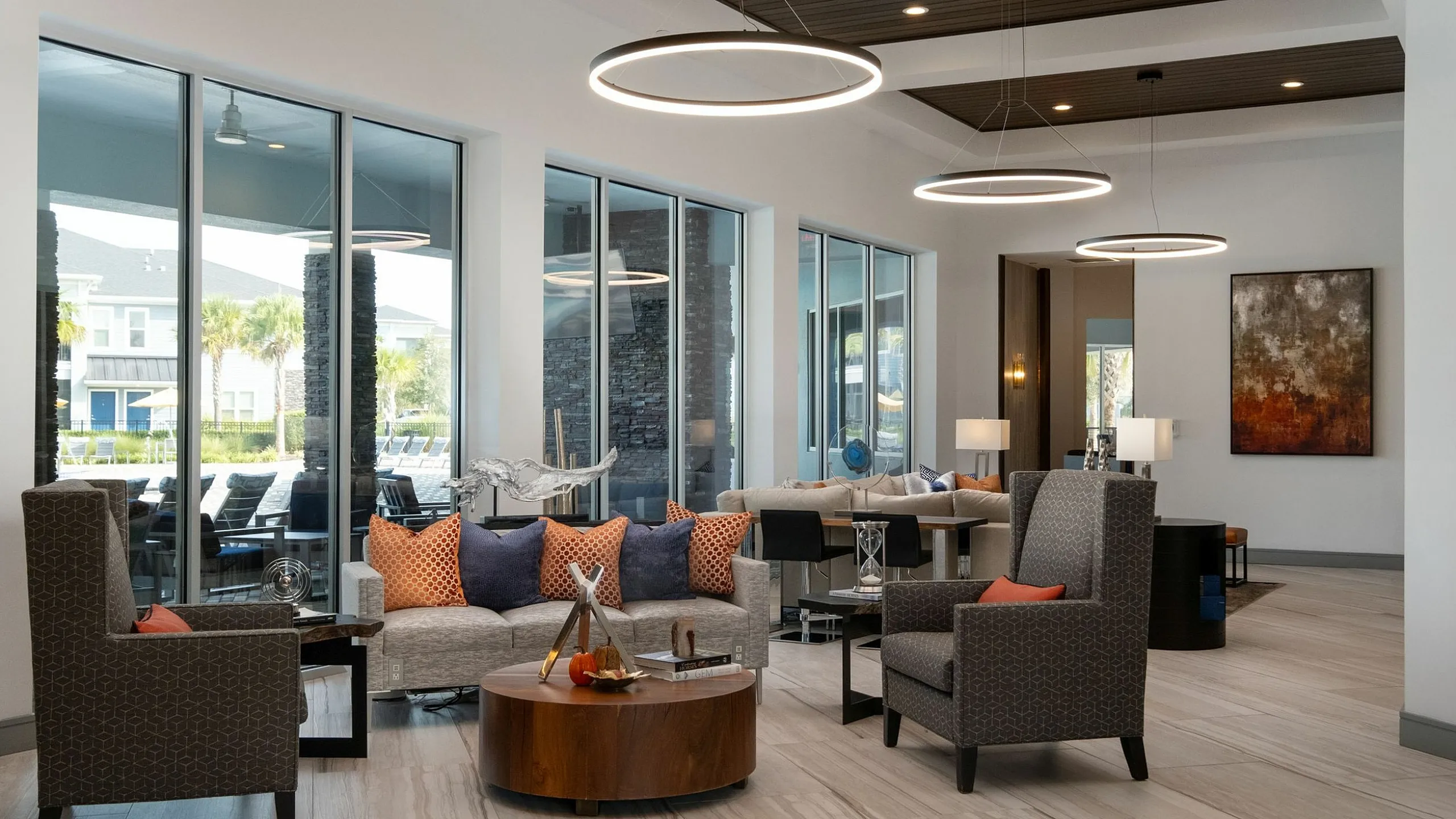 Elegant modern living area with cozy seating, stylish decor, and floor-to-ceiling windows offering a view of palm trees and a pool.