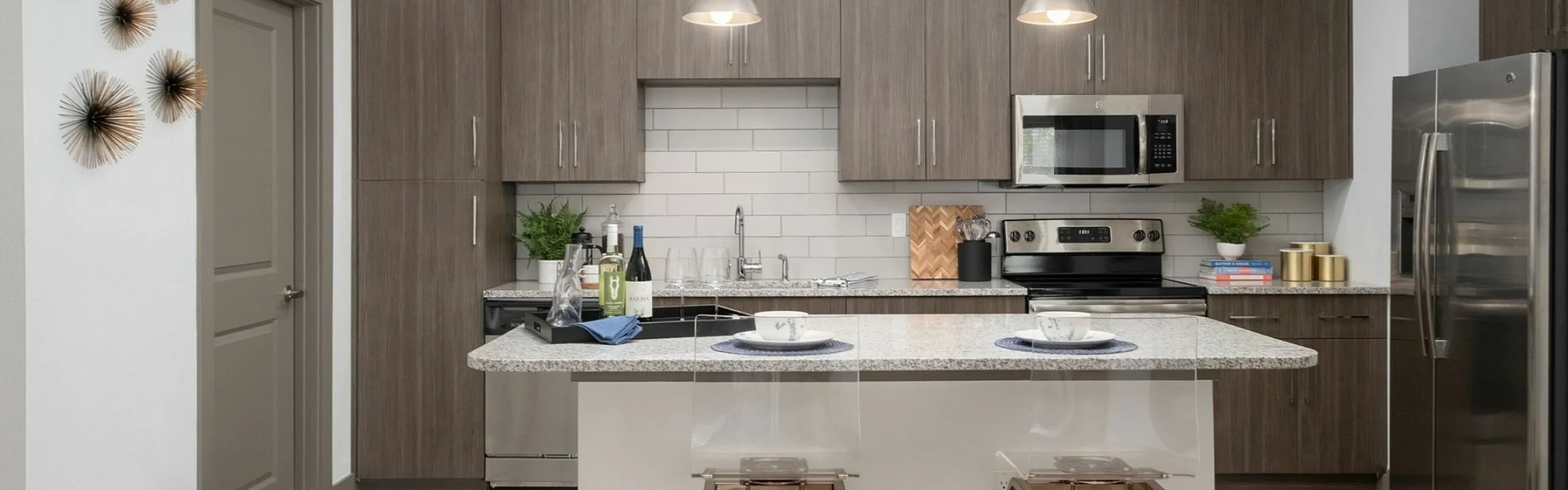 Modern kitchen with sleek wooden cabinetry, stainless steel appliances, and a chic breakfast bar island with stylish bar stools under pendant lighting.