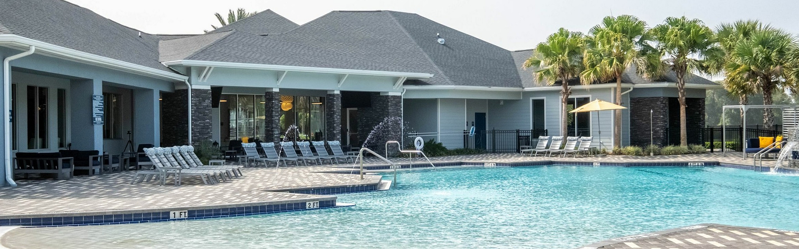 Inviting outdoor pool area with lounge chairs, modern clubhouse, and lush palm trees in a serene community setting.