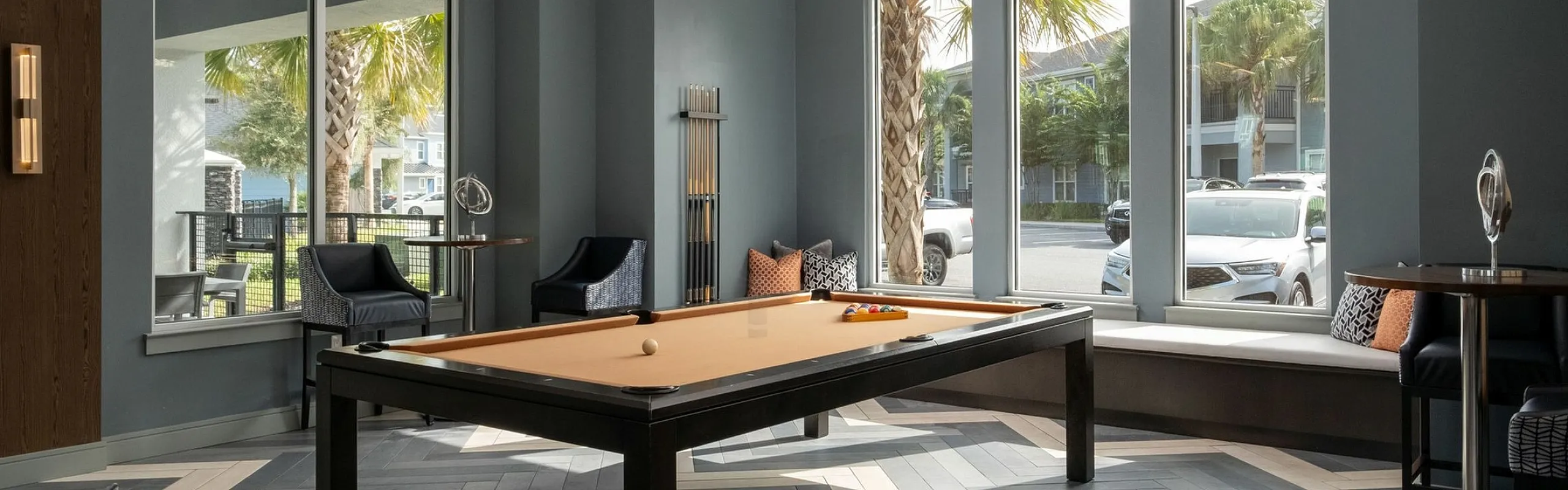 Luxurious modern lounge with a chic pool table, plush seating, and large windows overlooking palm trees.