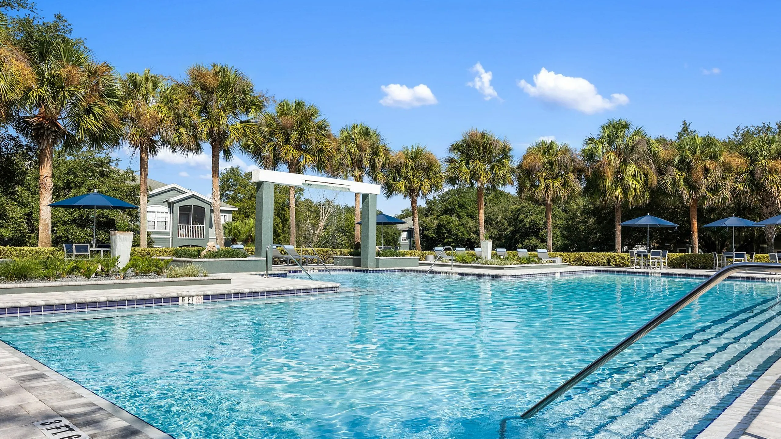Luxurious outdoor swimming pool surrounded by lush palm trees and clear blue skies, offering a perfect leisure spot.