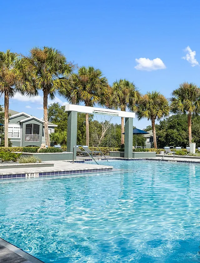 Luxurious outdoor pool area surrounded by palm trees with a clear blue sky, perfect for relaxation and leisure.