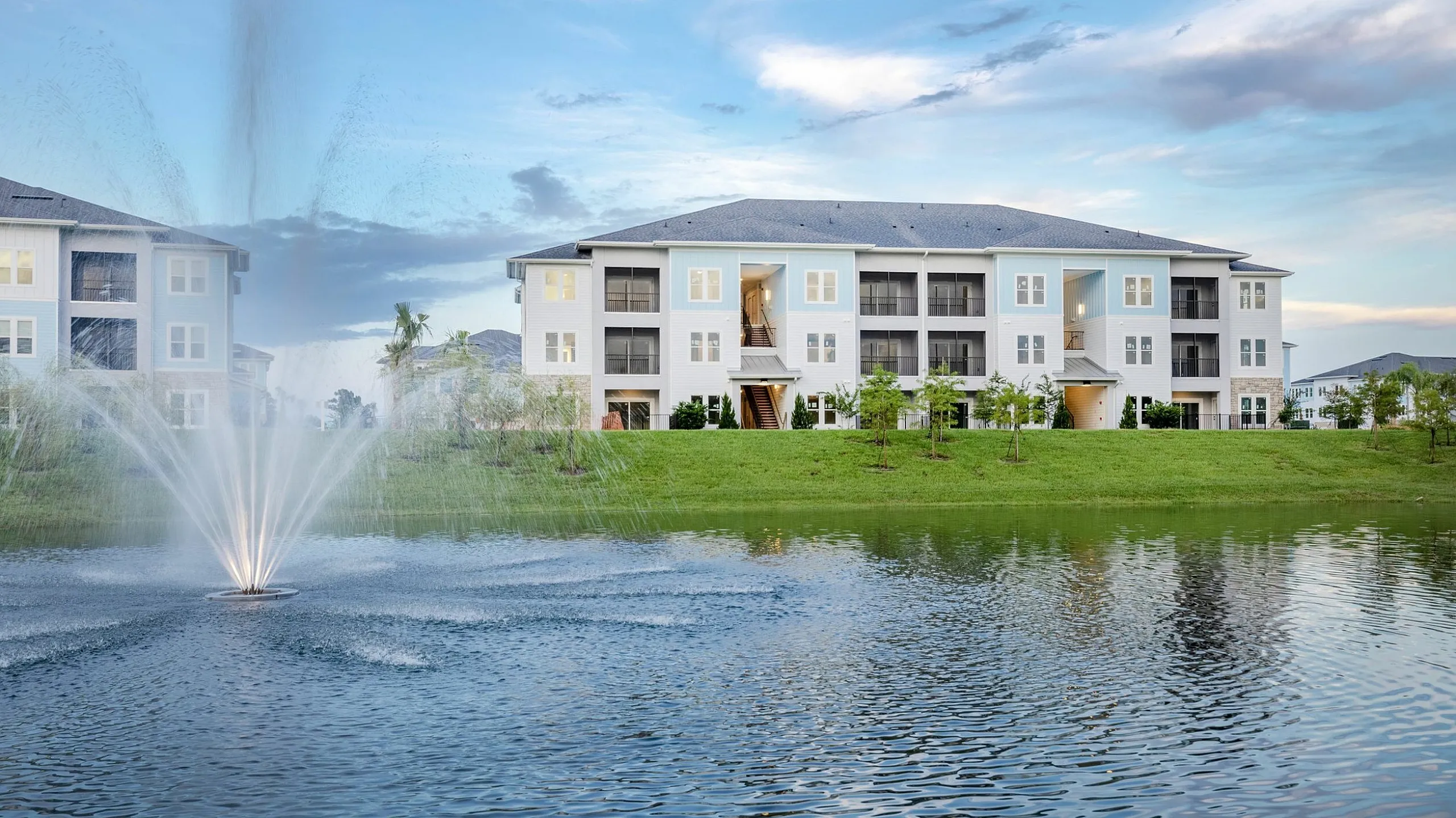 Charming apartment building with serene lake view and vibrant water fountain display.