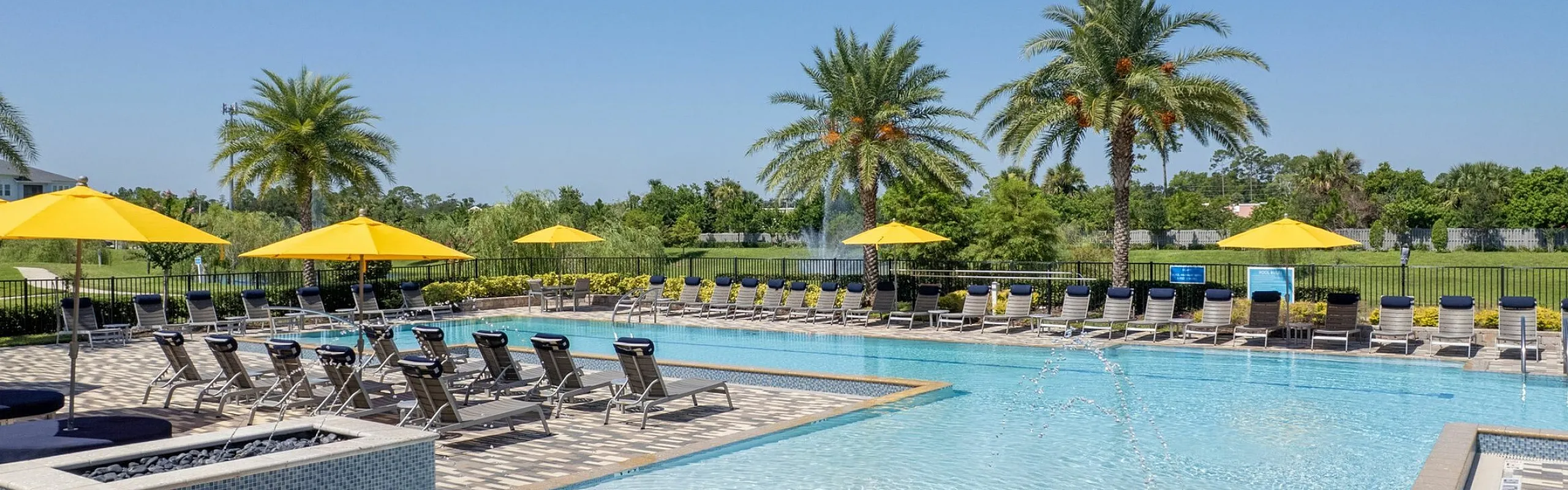 Luxurious resort-style swimming pool with palm trees, sun loungers, and vibrant yellow umbrellas creating a relaxing oasis.