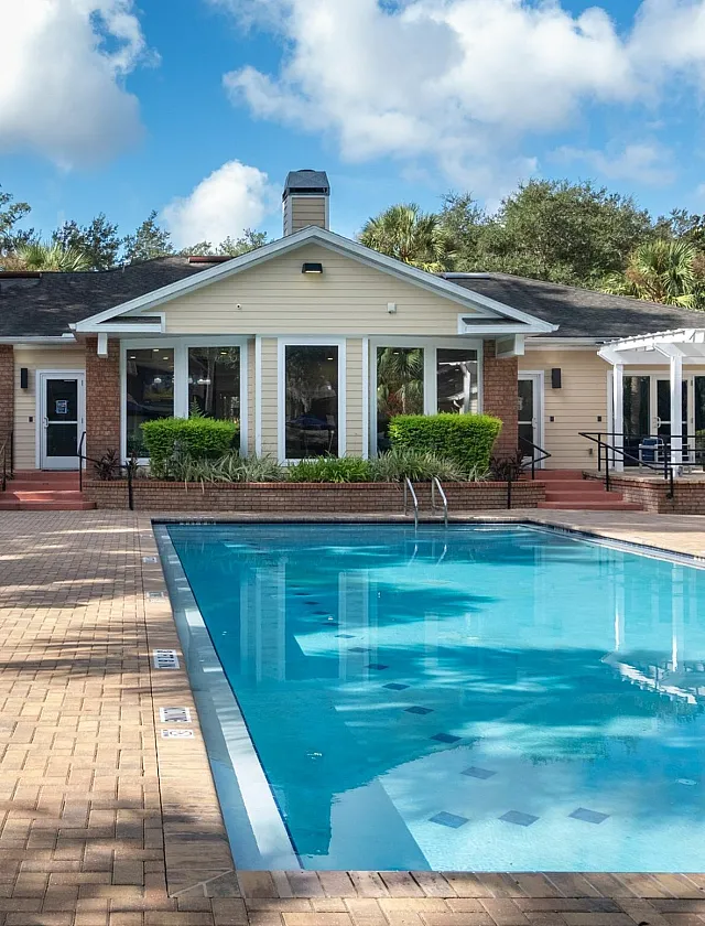Luxurious apartment complex featuring a sparkling pool, surrounded by stylish loungers and umbrellas, set against a backdrop of lush greenery.