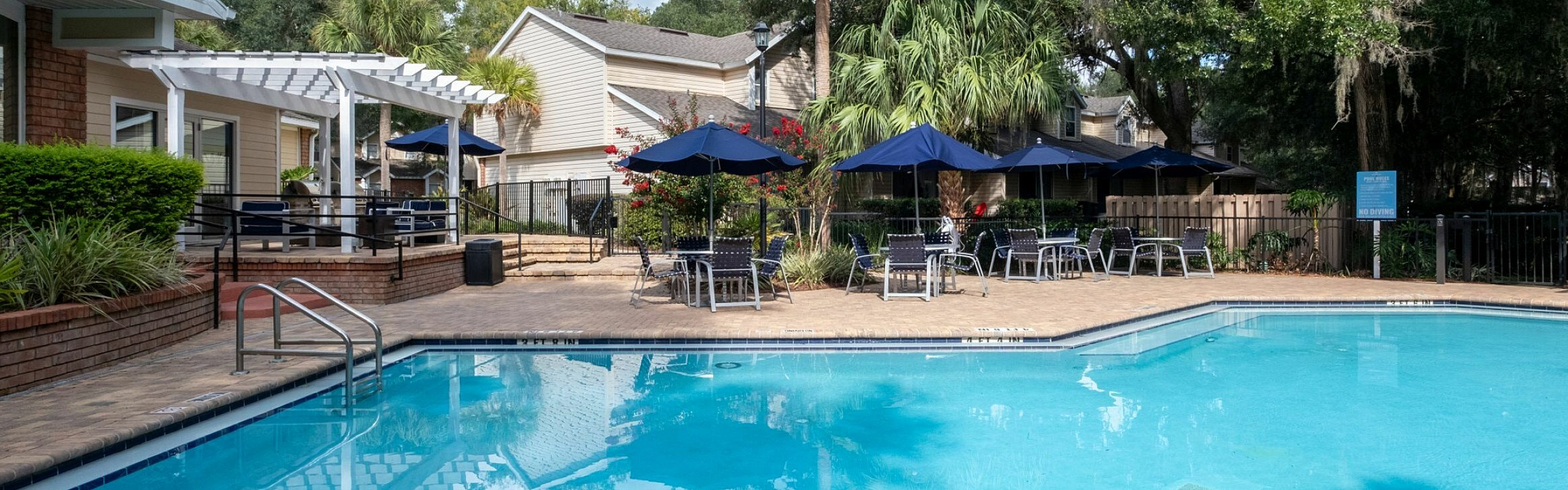 Inviting outdoor pool area with lush greenery, comfortable seating, and elegant pergola under a vibrant blue sky.
