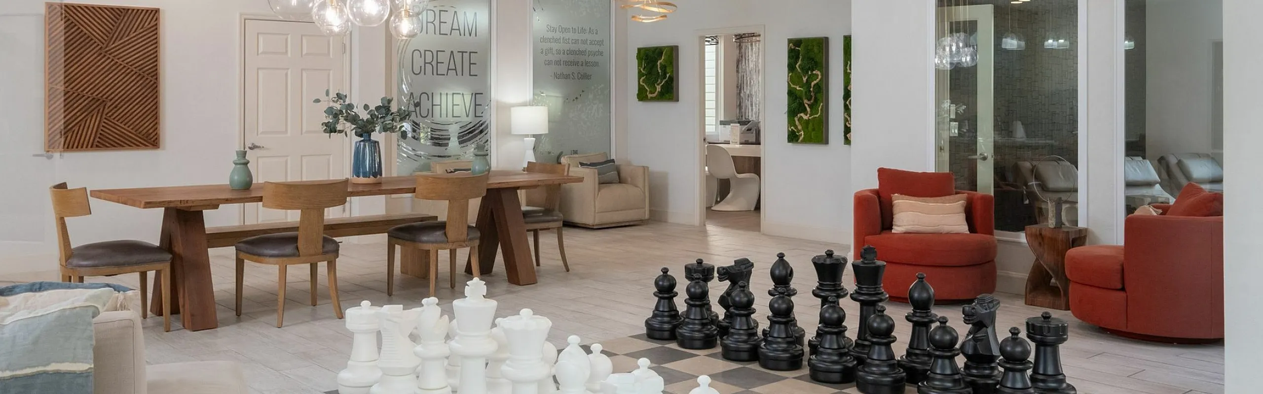 Elegant and spacious open-plan living area featuring modern lighting, a large dining table, cozy seating, and a unique giant chess set centerpiece.