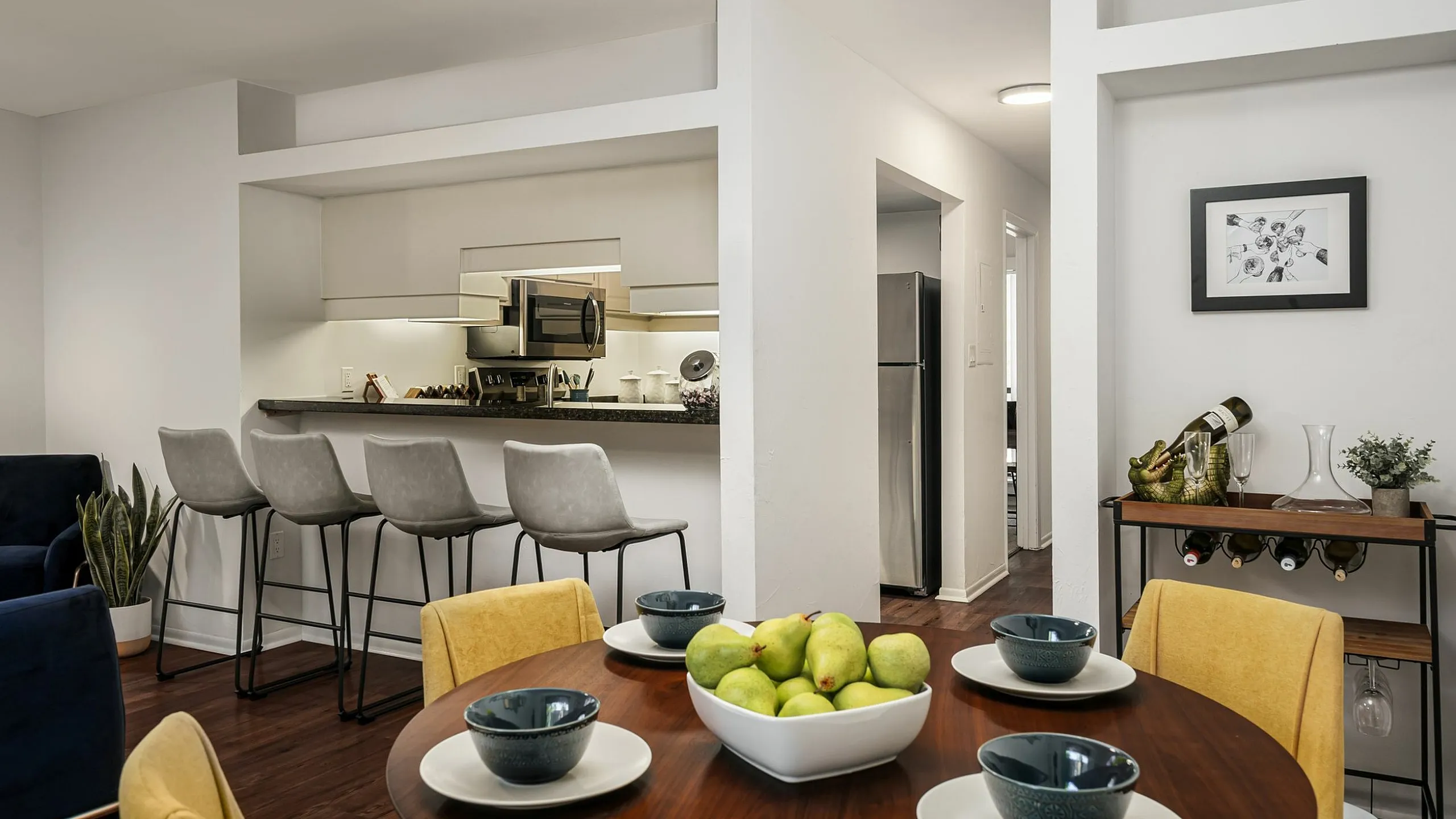 Modern apartment dining area with elegant bar seating, stylish kitchen, and vibrant decor featuring a fruit centerpiece.