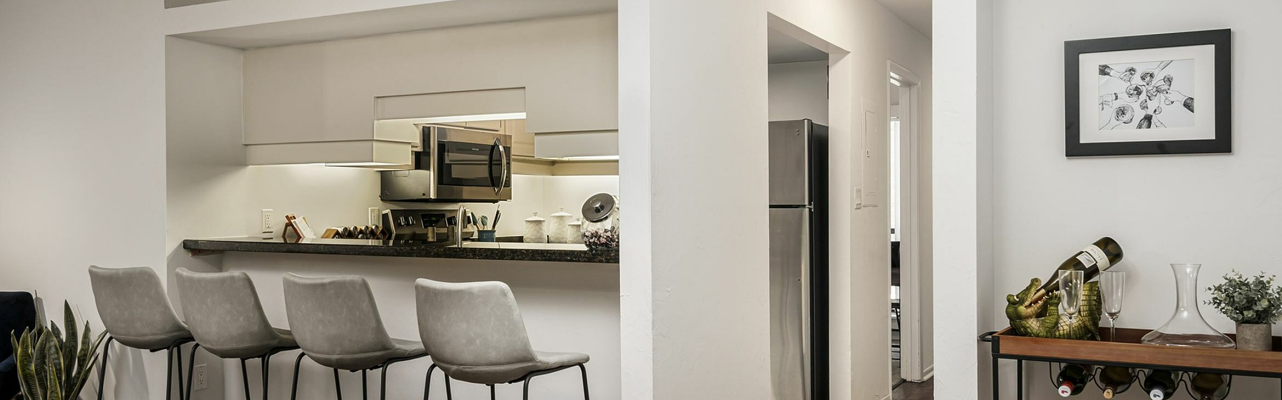 Modern apartment interior featuring a stylish open kitchen with sleek countertops, elegant bar stools, and a cozy dining area set with colorful chairs and decorative details.