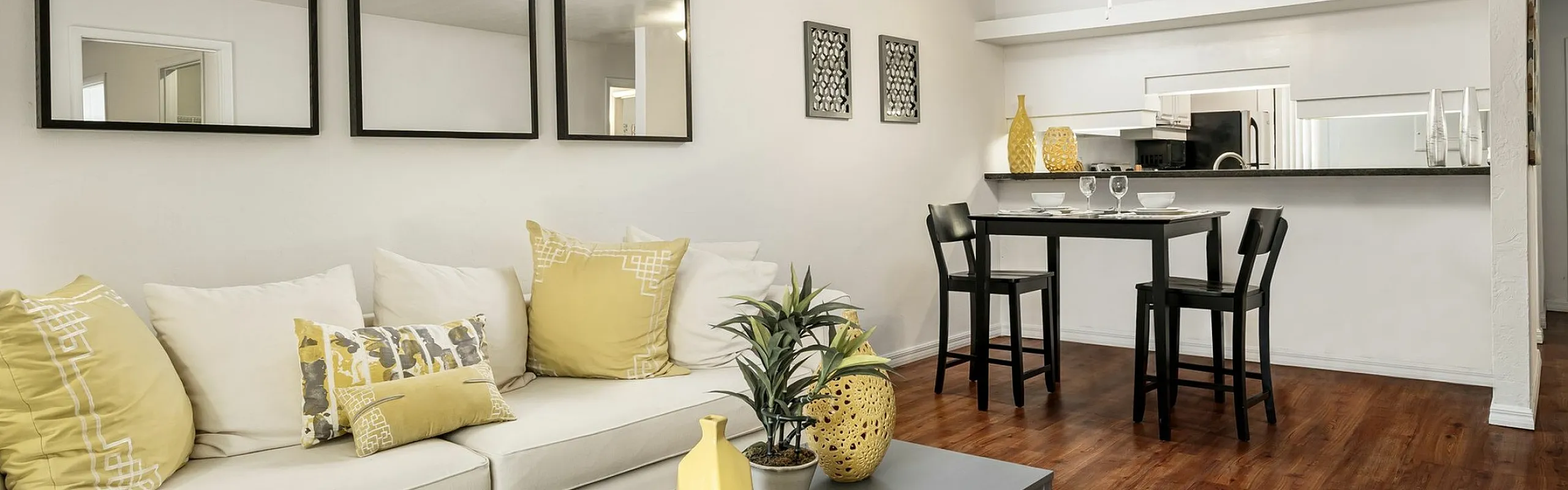 Inviting living area featuring a cozy white sofa with yellow accents, stylish wooden flooring, and a sleek dining space next to an open kitchen.