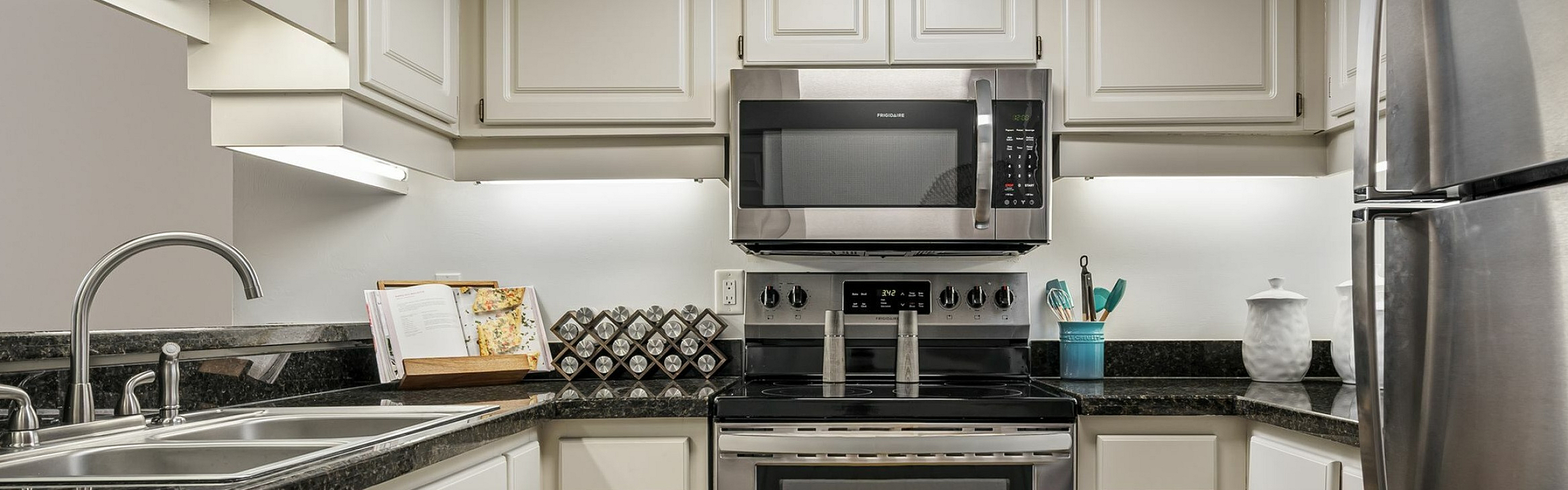 Modern kitchen with stainless steel appliances, sleek black countertops, and classic white cabinetry.