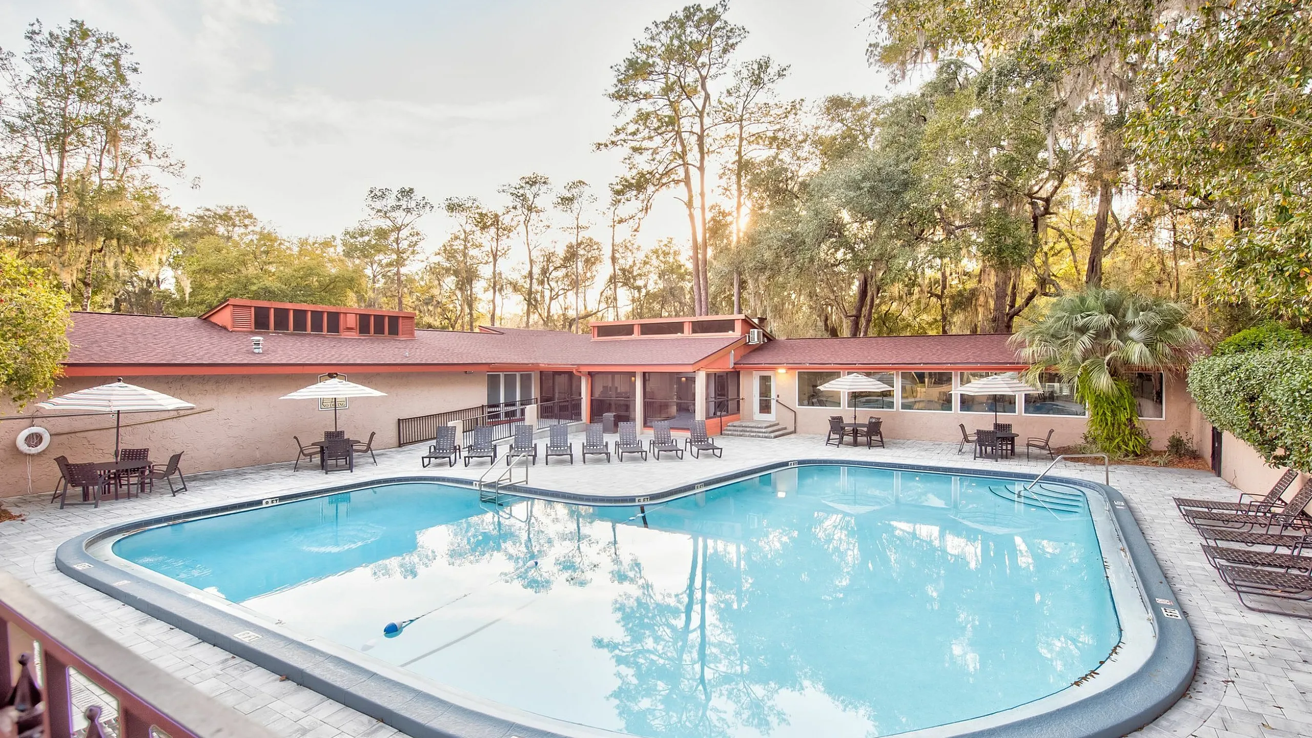 Inviting outdoor pool area surrounded by lush trees, featuring lounge chairs and umbrella-shaded tables, perfect for relaxing afternoons.