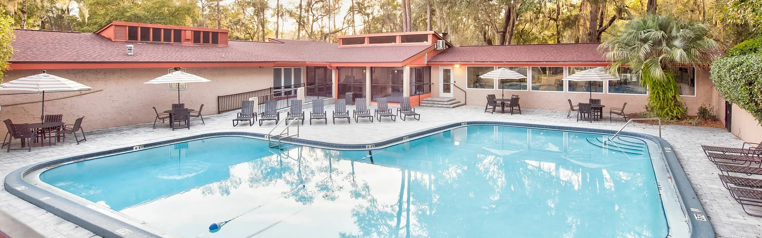 Charming community pool area surrounded by lush greenery and elegant patio seating, perfect for relaxation and entertaining.