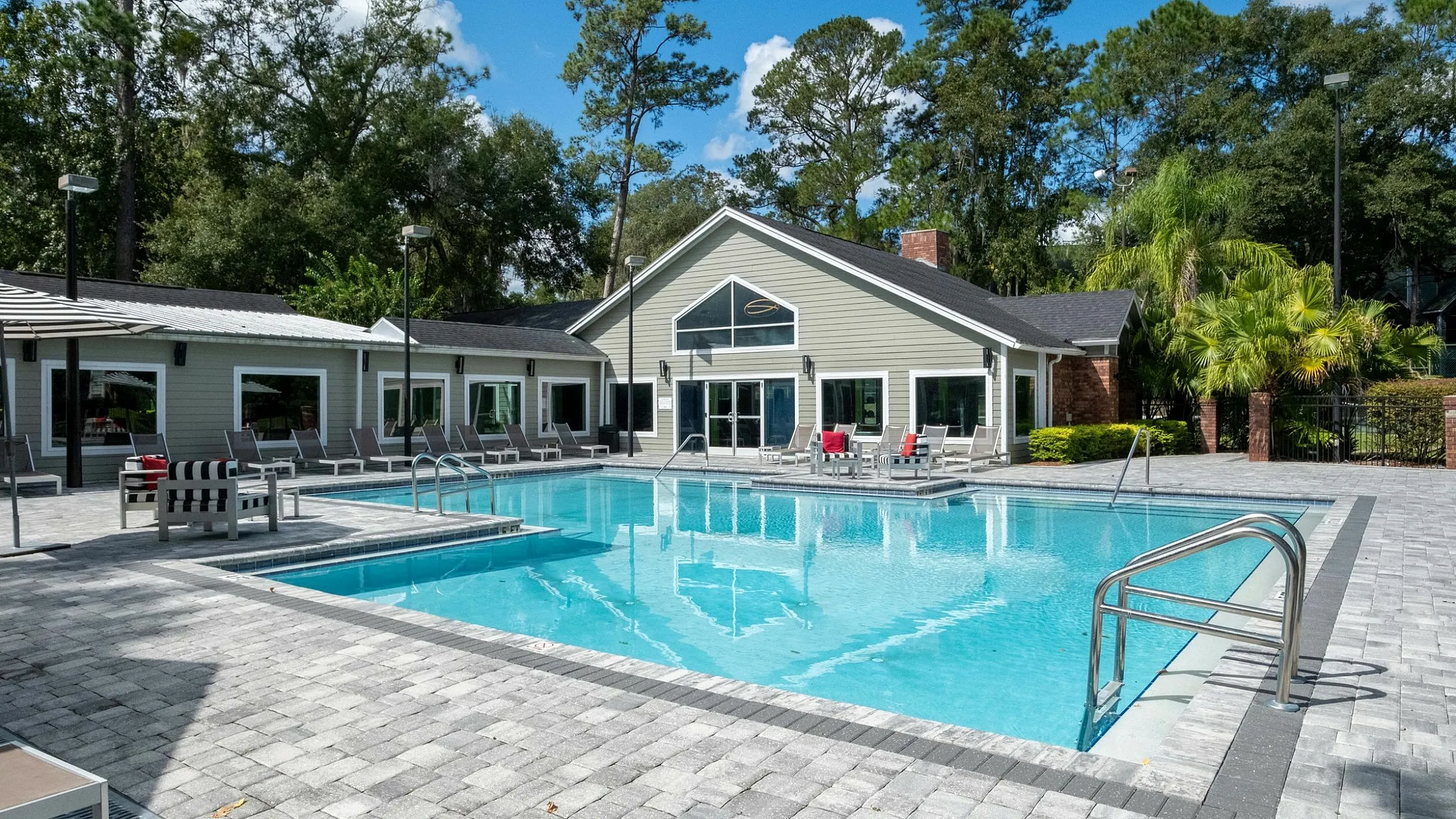 Luxury apartment complex with a stunning outdoor pool surrounded by stylish lounge chairs, nestled in a serene setting with lush greenery.