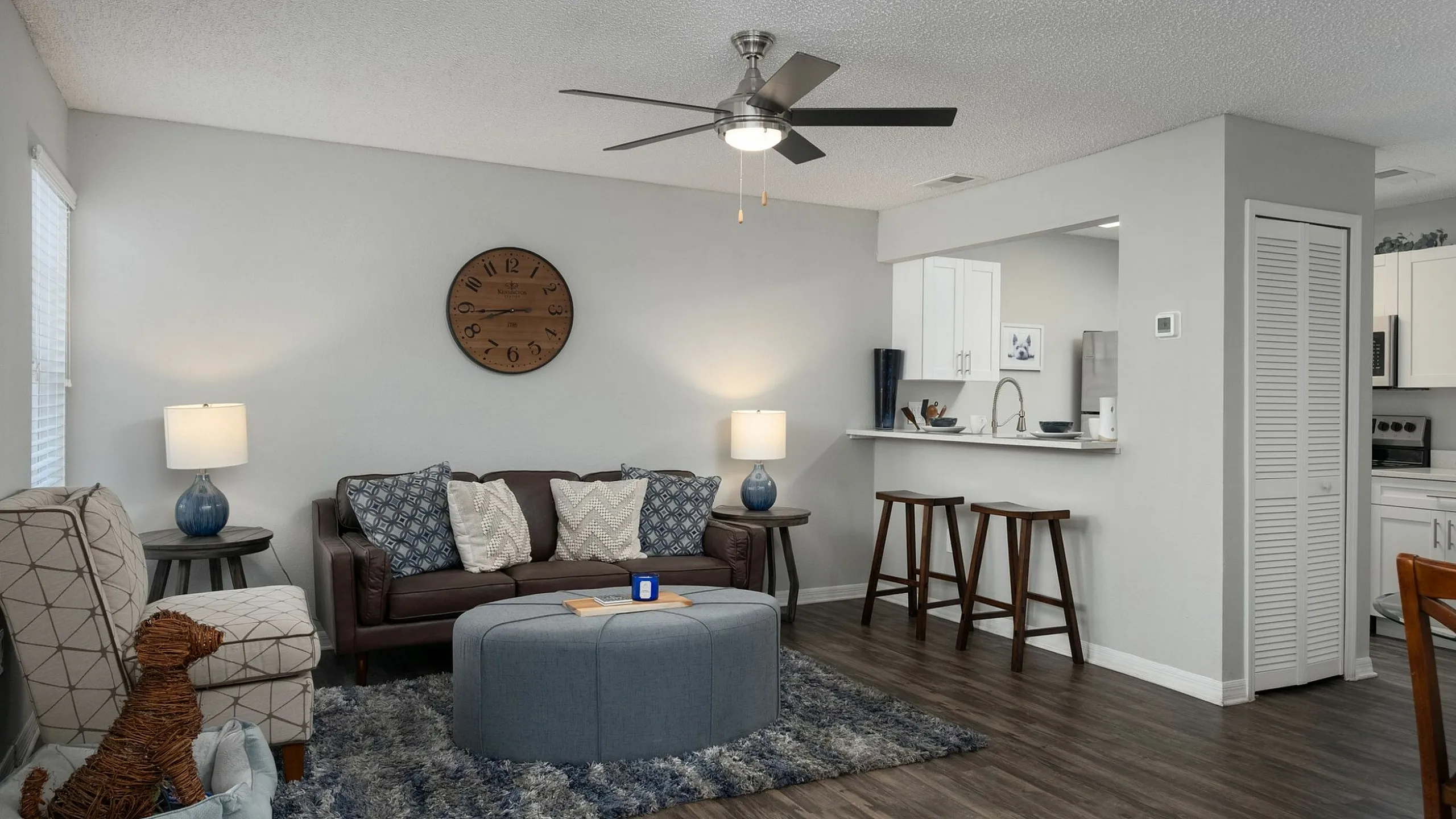 Inviting open-concept living area with stylish decor, featuring a cozy couch, plush armchair, and modern ceiling fan, adjacent to a chic kitchen with a convenient breakfast bar.