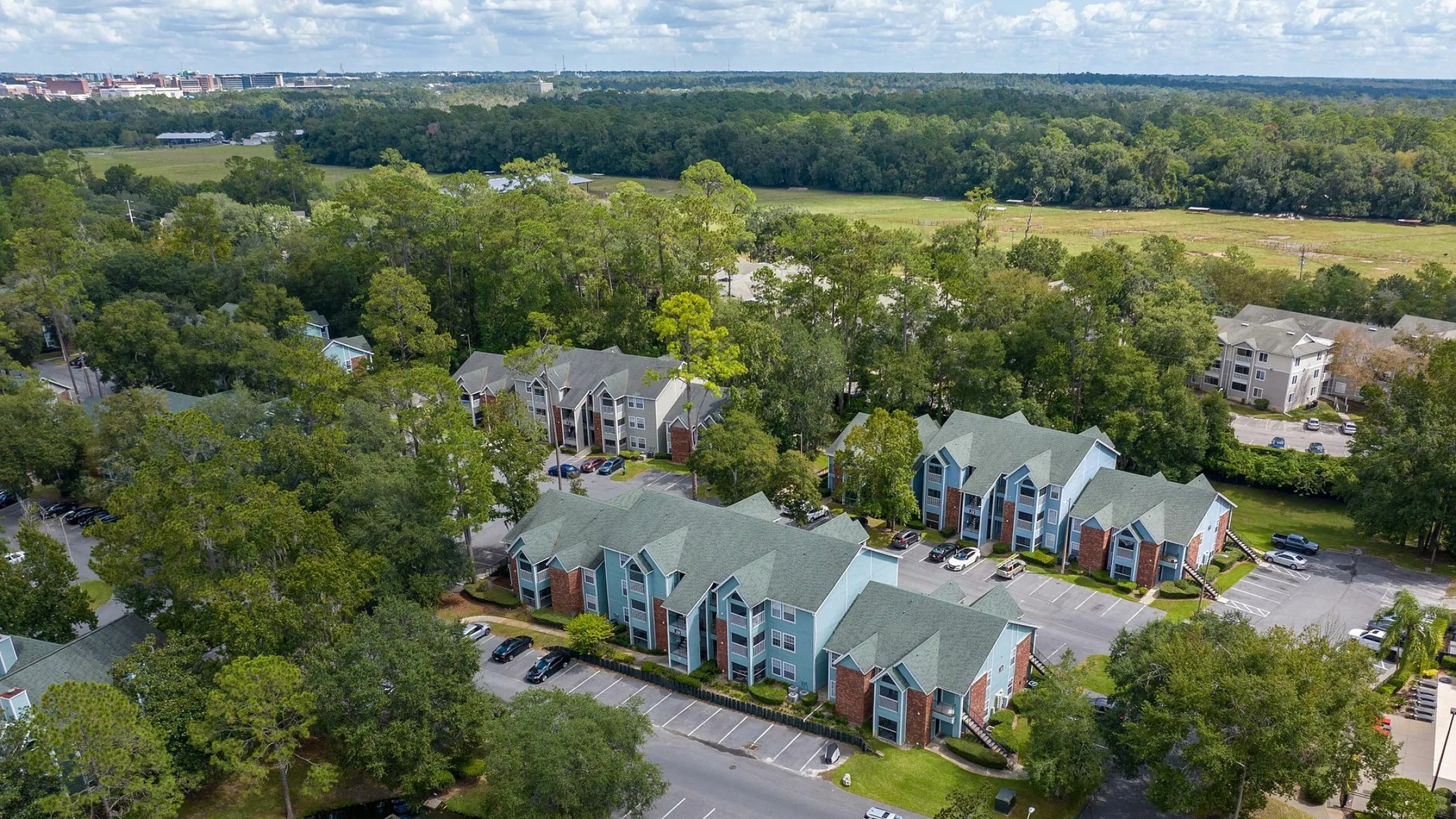 Scenic aerial view of modern apartment complex nestled among lush greenery, featuring a tranquil pond and ample parking.
