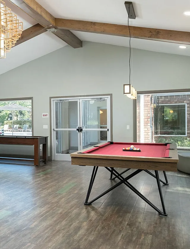Bright and airy recreation room featuring a modern pool table, sleek bar area with high chairs, and large windows allowing natural light.