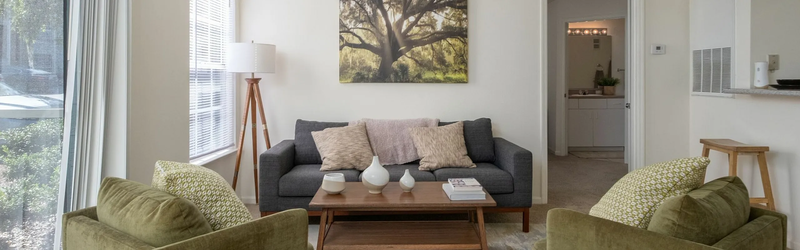 Inviting living room with modern decor, featuring a cozy gray sofa, olive green armchairs, and a scenic window view enhancing the bright, open space.