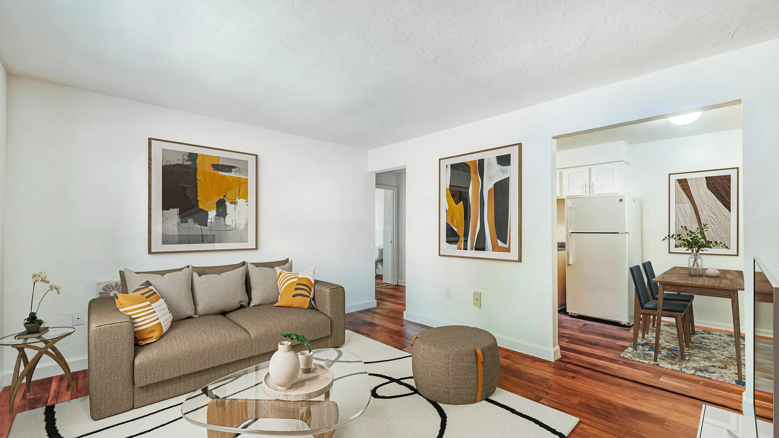 Chic living space with modern decor, featuring a cozy sofa, abstract wall art, and an elegant open layout flowing into a compact kitchen area.
