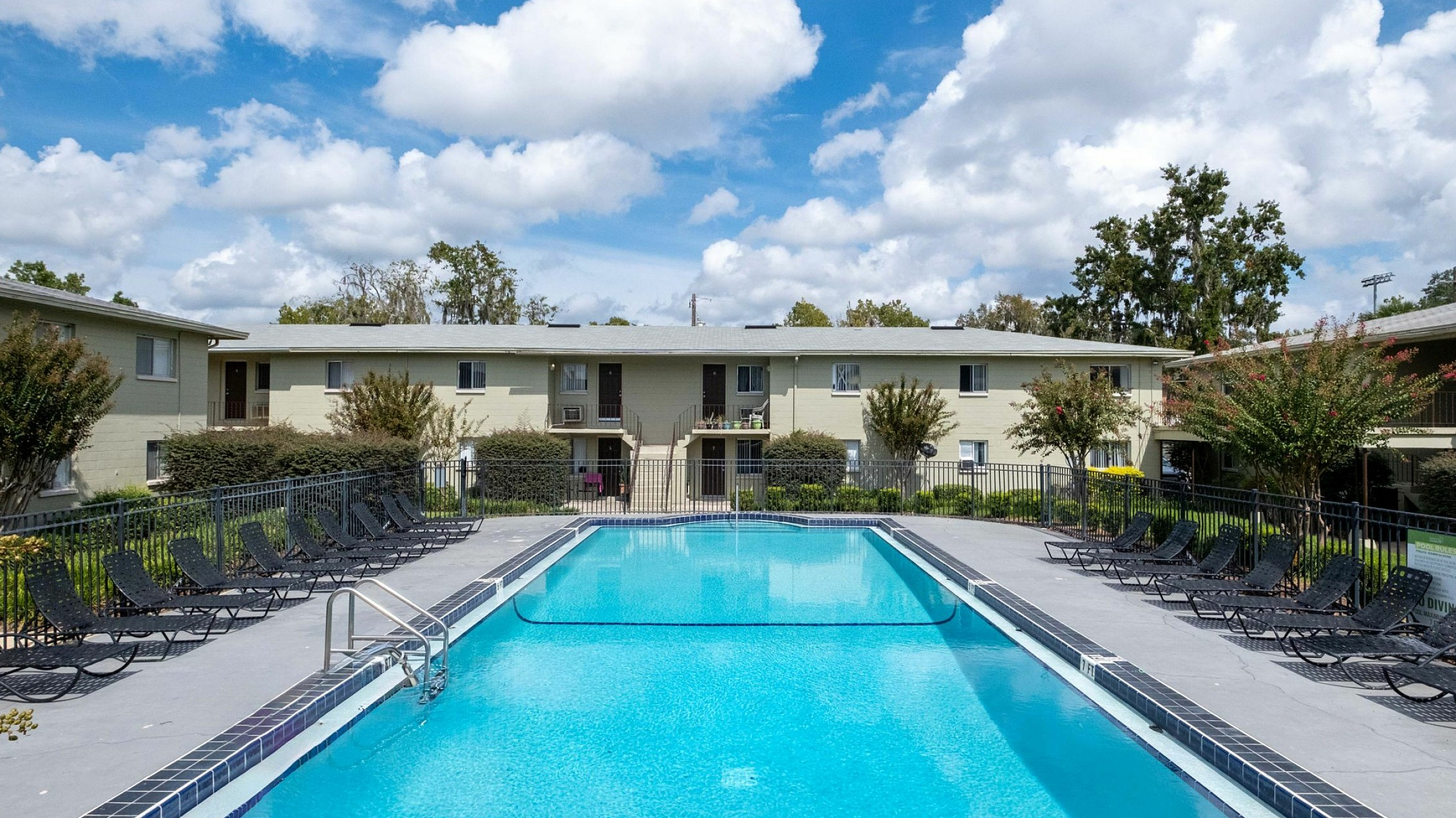 Inviting apartment complex featuring a sparkling swimming pool surrounded by lush greenery and sun loungers for ultimate relaxation.