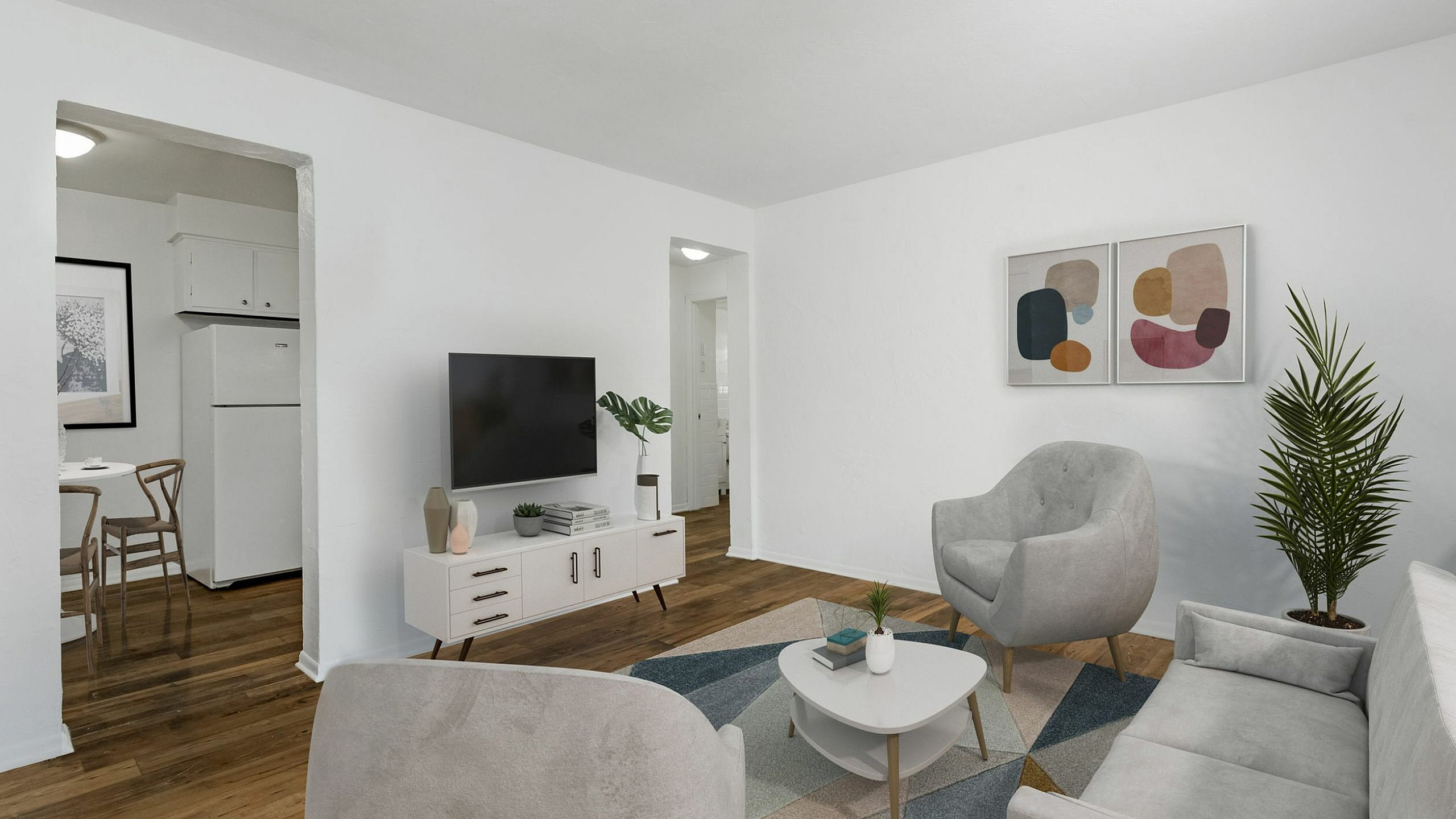 Chic and cozy living room with modern decor, featuring plush seating, elegant artwork, and a stylish media console. Open view towards a quaint dining area with natural wood elements.