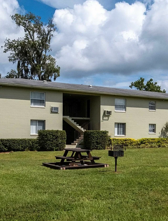 Charming apartment building with a lush green lawn, picnic area, and serene surroundings, perfect for relaxation and outdoor enjoyment.