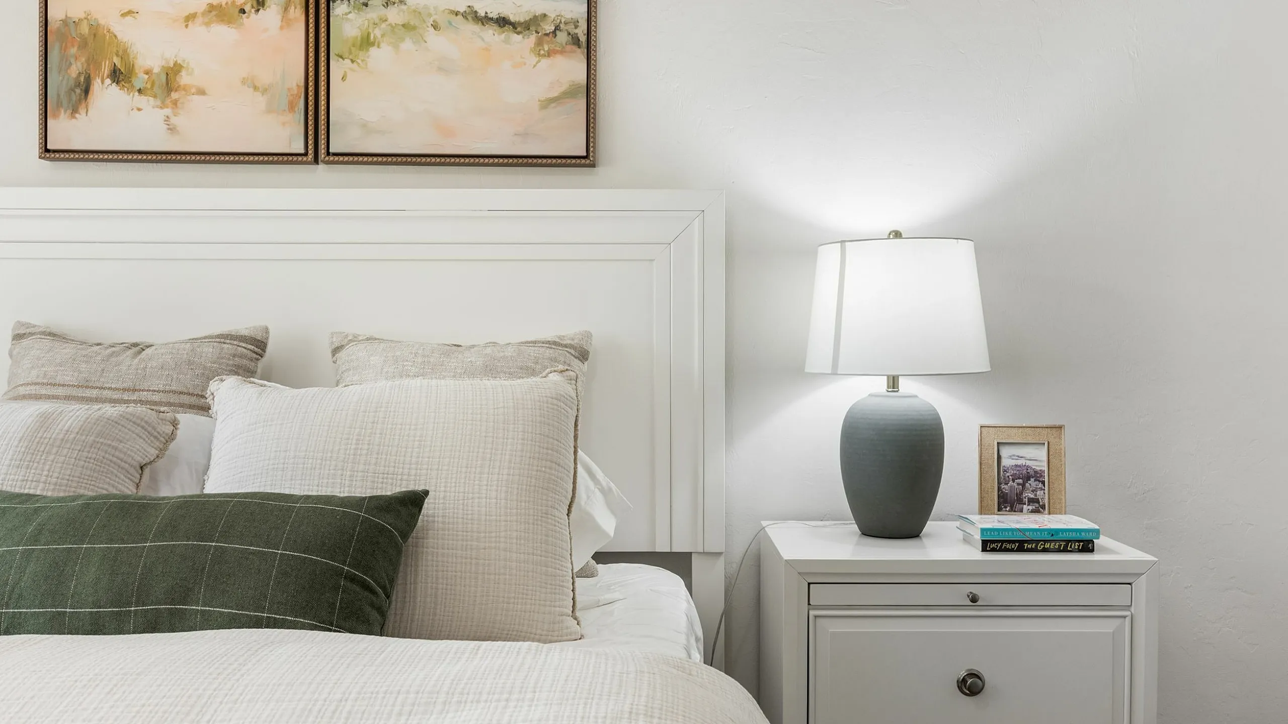 Cozy bedroom with elegant white bedding, accent pillows, and soft lighting from an elegant bedside lamp.