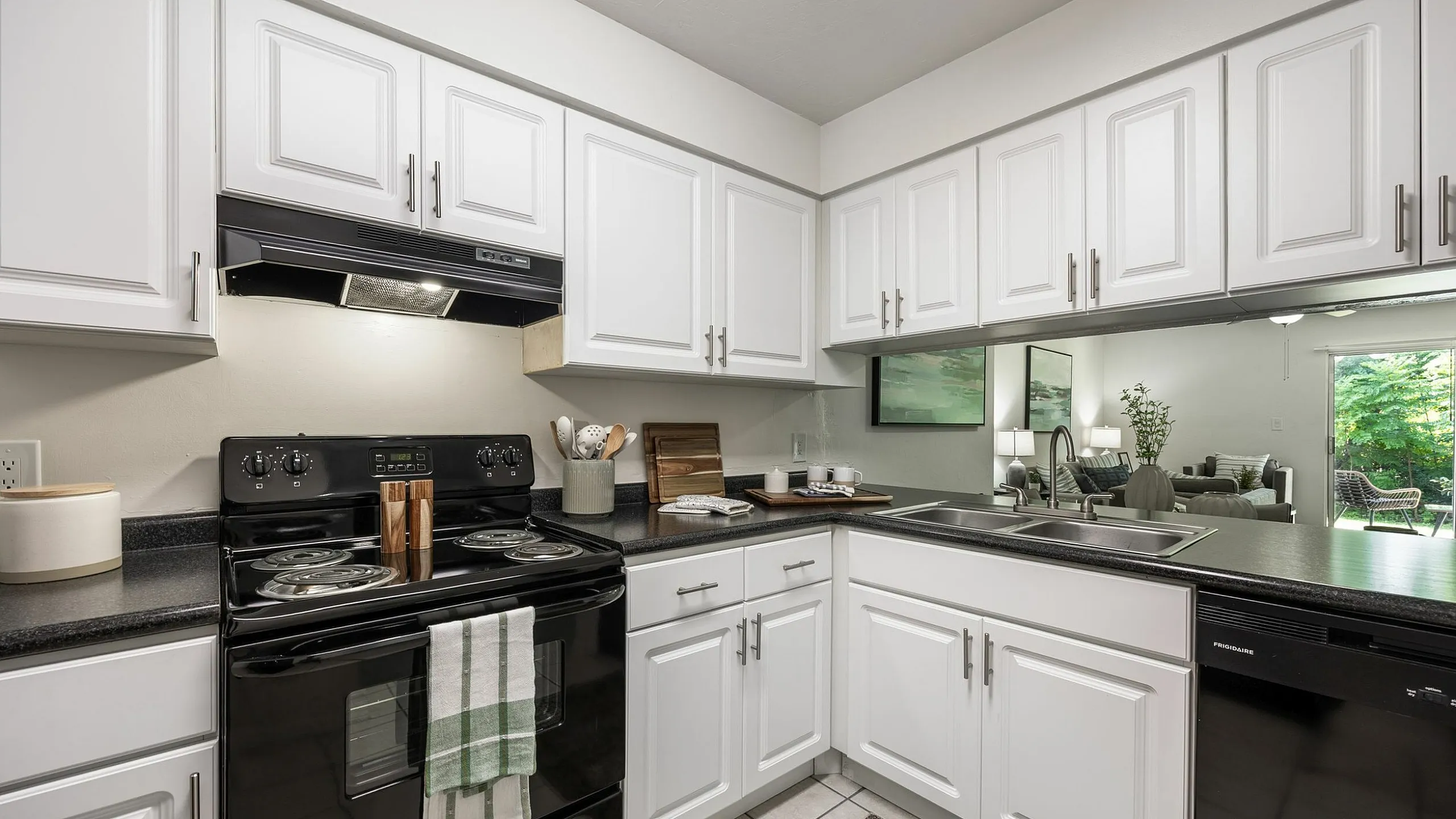 Inviting kitchen with elegant white cabinetry, modern black appliances, and a cozy glimpse into a sunlit living area.