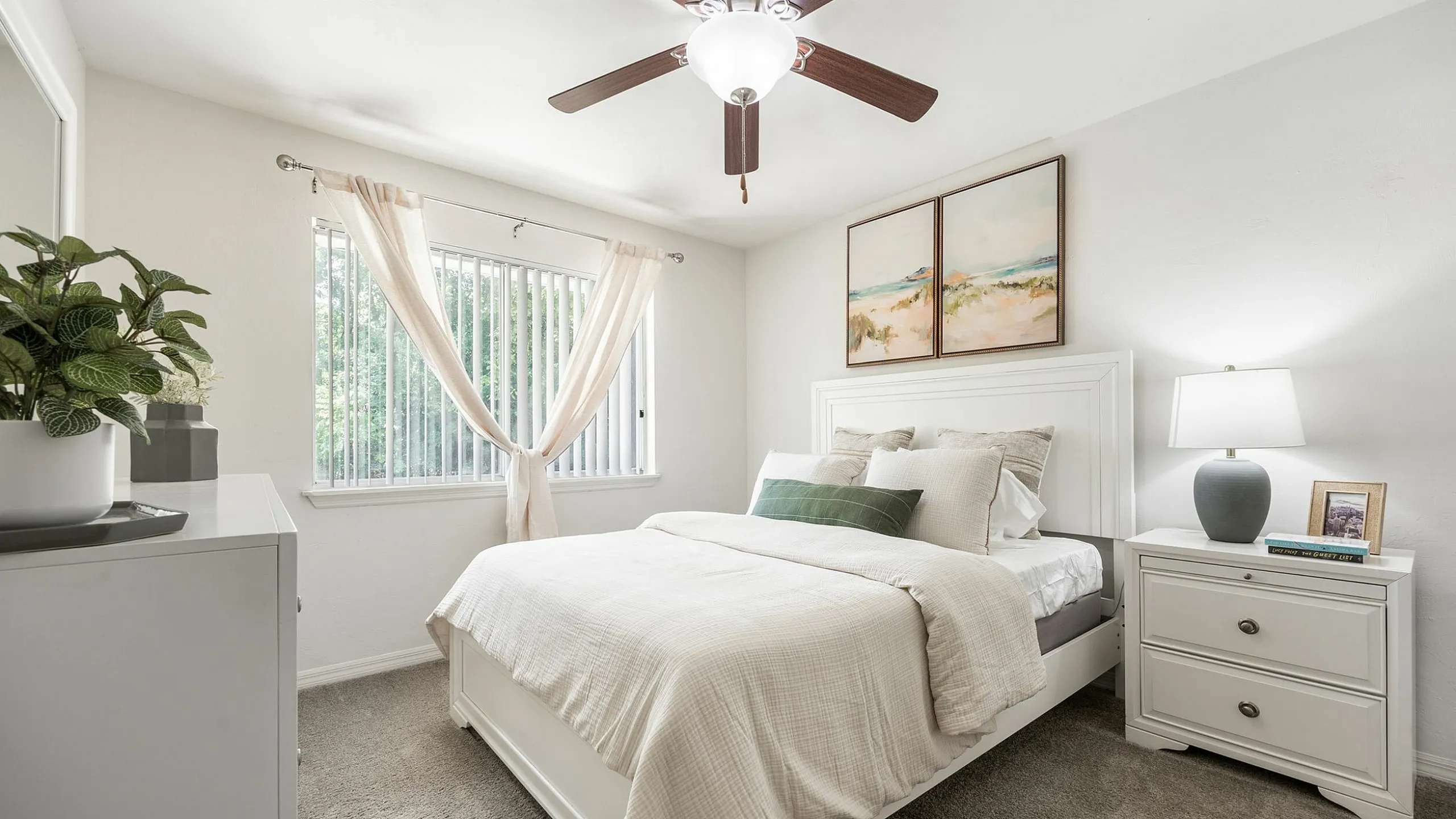 Bright and welcoming bedroom with natural light, featuring a cozy white bed, elegant ceiling fan, and tasteful decor.