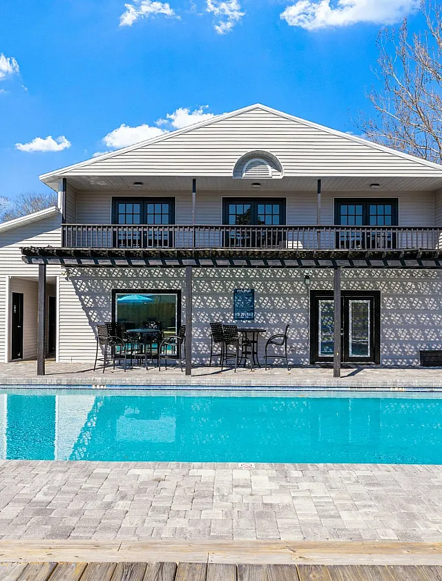 Charming two-story home featuring a sunlit patio, inviting swimming pool, and elegant outdoor seating area, perfect for relaxation.