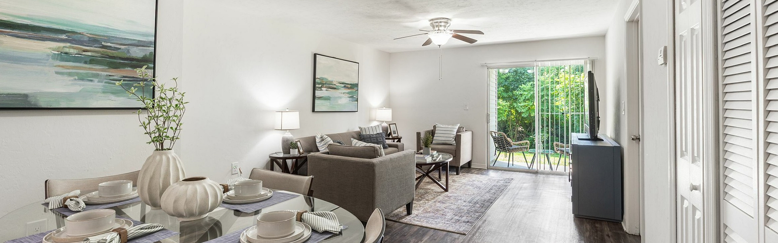 Bright and inviting open-concept living space with modern dining set, cozy seating area, and large glass doors leading to a lush green patio.