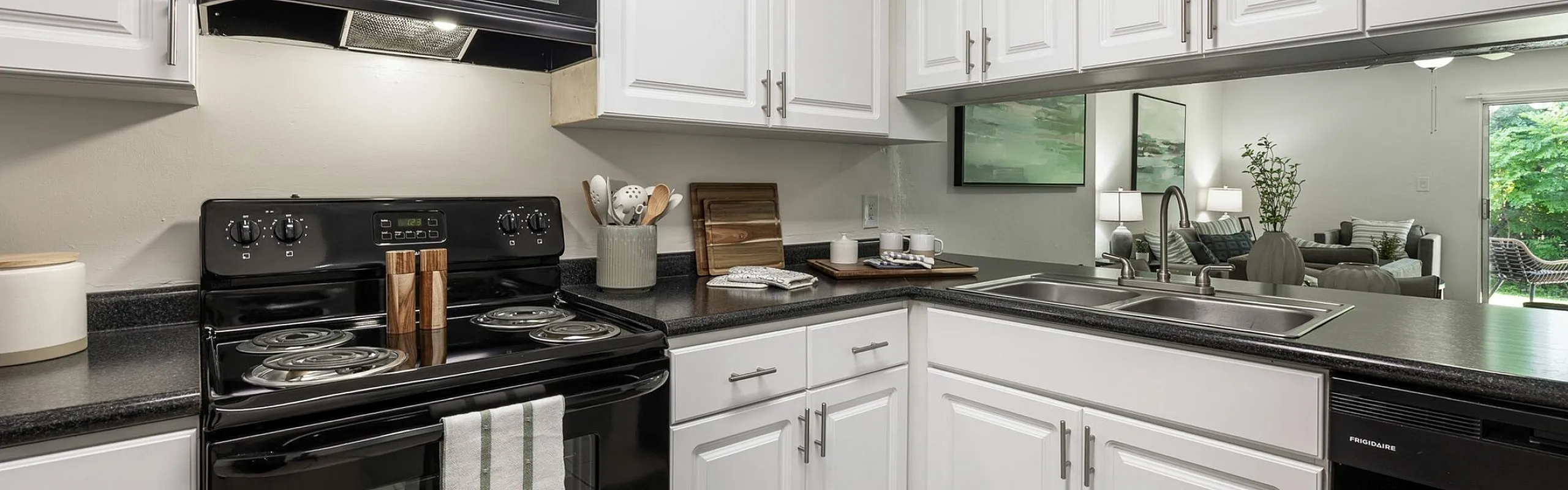 Modern kitchen with sleek black appliances, white cabinetry, and an inviting open layout leading to a bright living area with garden views.