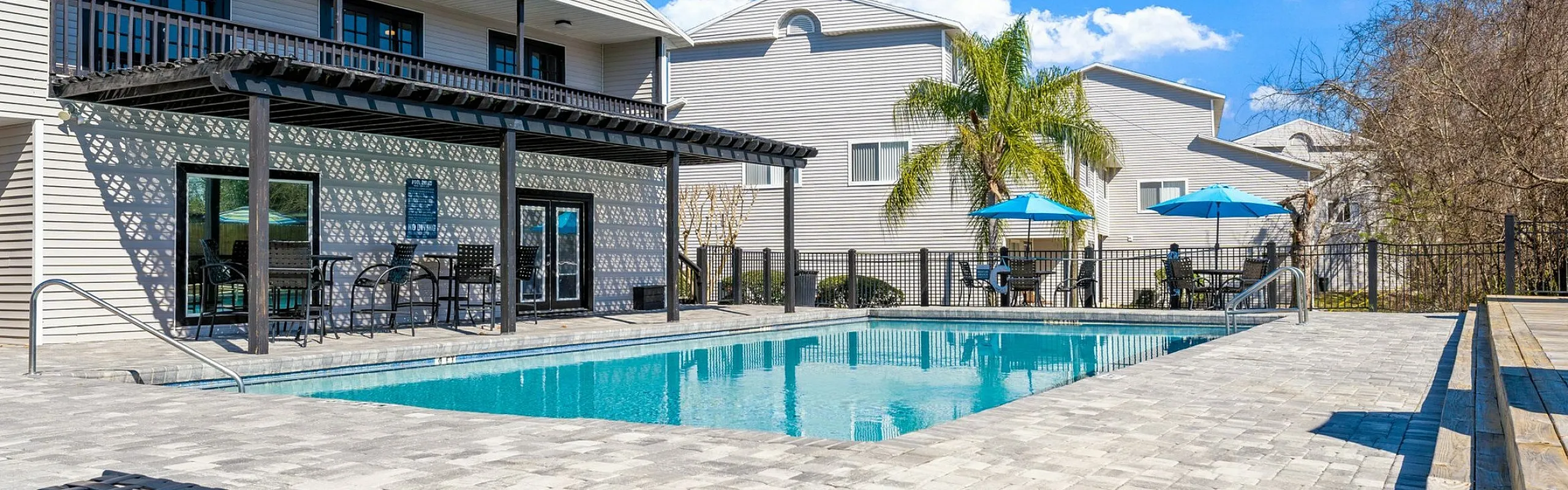 Charming apartment complex with a sparkling pool, surrounded by sun chairs and lush palm trees, perfect for outdoor relaxation.