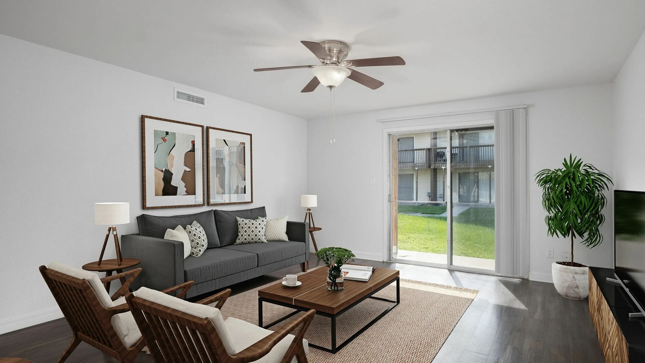 Bright and modern living room with sleek wooden flooring, cozy gray sofa, stylish armchairs, and a large glass door opening to a lush green view.