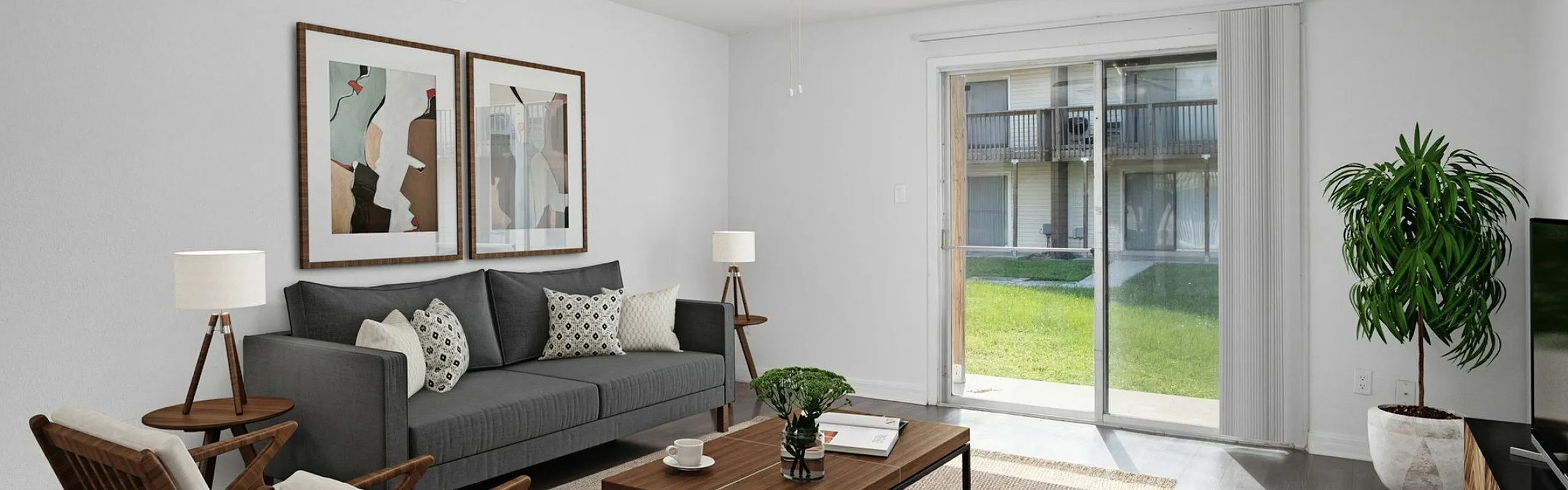 Inviting living room with modern decor, featuring a cozy gray sofa, stylish wooden chairs, vibrant artwork, and large sliding glass doors opening to a lush outdoor view.