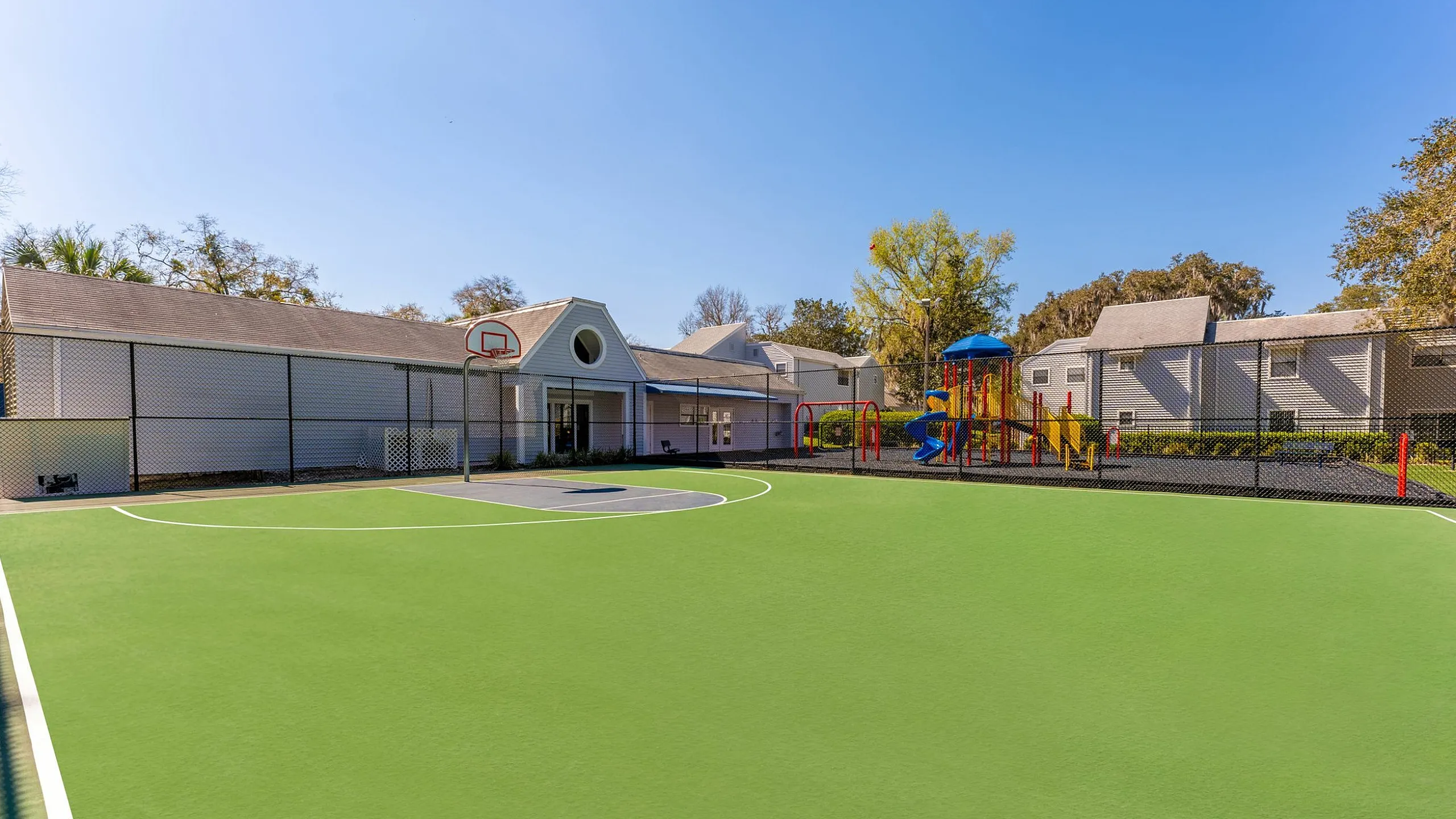 Vibrant community area featuring a sunlit basketball court and colorful playground, perfect for active family living.