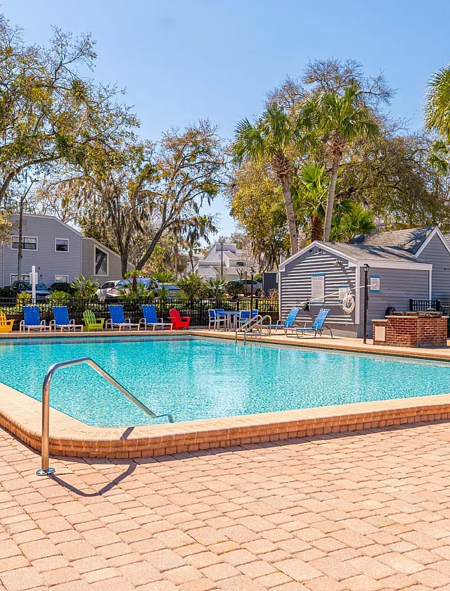 Vibrant outdoor pool area with colorful lounge chairs, surrounded by lush greenery and modern residential buildings.