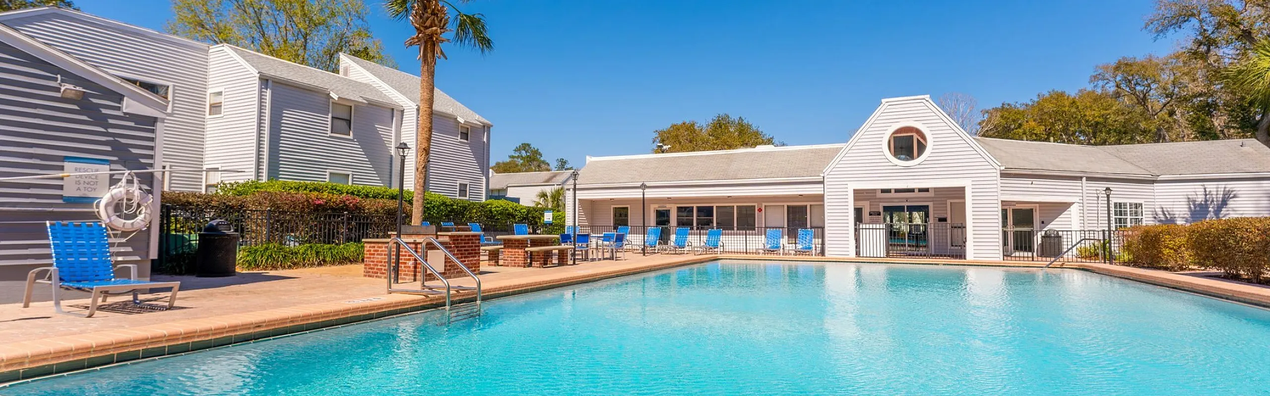 Inviting residential complex featuring a sparkling swimming pool, sunny patio seating, and modern architecture under a clear blue sky.