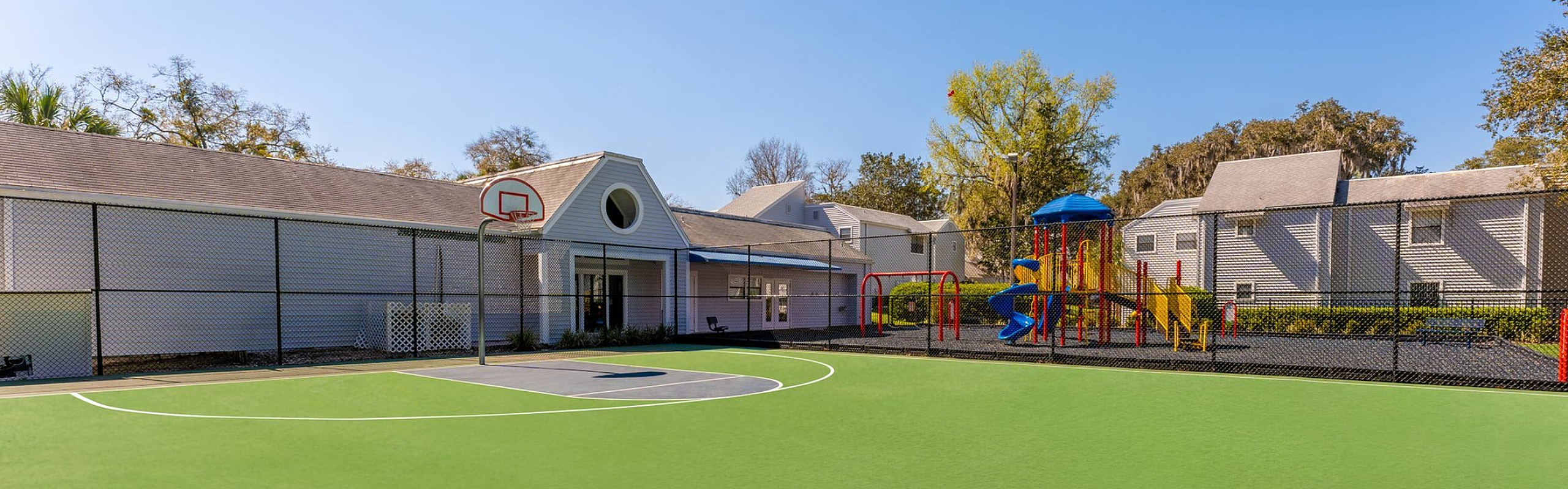 Charming apartment amenities with a vibrant basketball court and colorful children's playground against a backdrop of cozy community buildings.