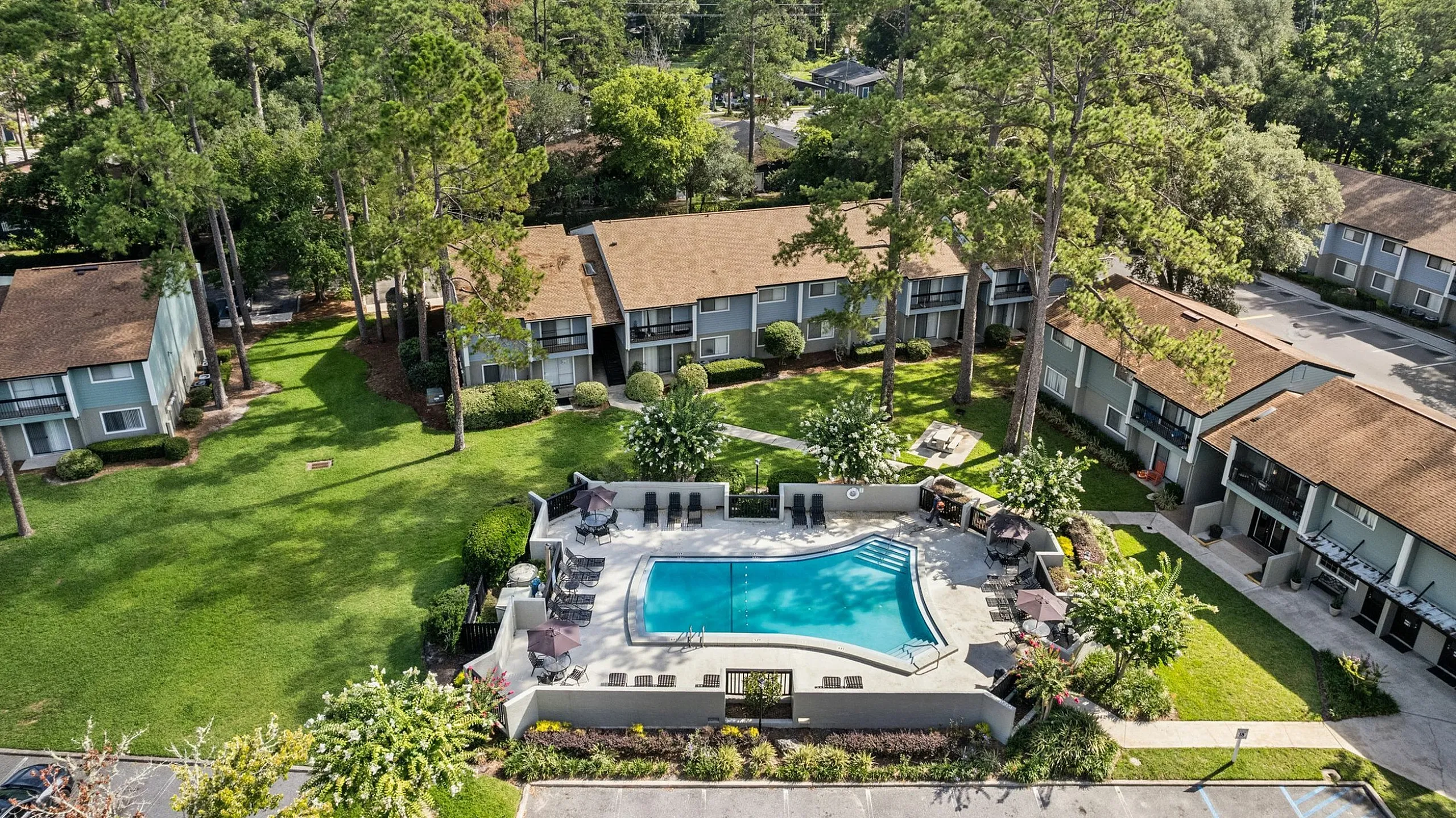 Serene aerial view of a beautifully landscaped apartment complex with a sparkling central swimming pool surrounded by lush greenery, ideal for a tranquil living experience.
